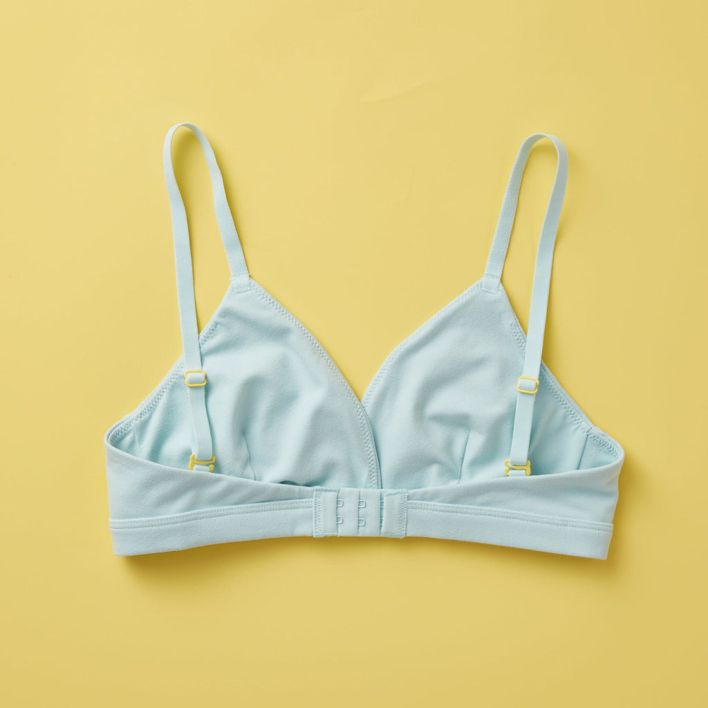 Yellowberry Butter Bra in light blue, back laydown image. The BEST Bra We Make for More Developed Girls. Fabric is smooth to the touch and made with a matte brushed finish for extra softness. Made with synthetic fabric blend and hook and eye clasp closure. Great for developing girls. Wear and wash is over and over again, it will still look brand new. It will grow with your daughter as she continues to grow, great option for any occasion.