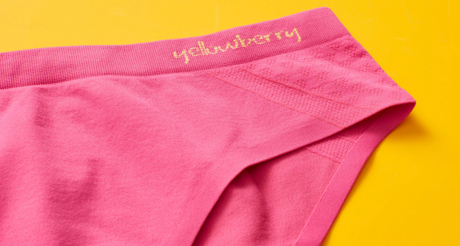 Close up image of watermelon pink seamless underwear laying on a yellow background with "yellowberry" embroidered on the garment