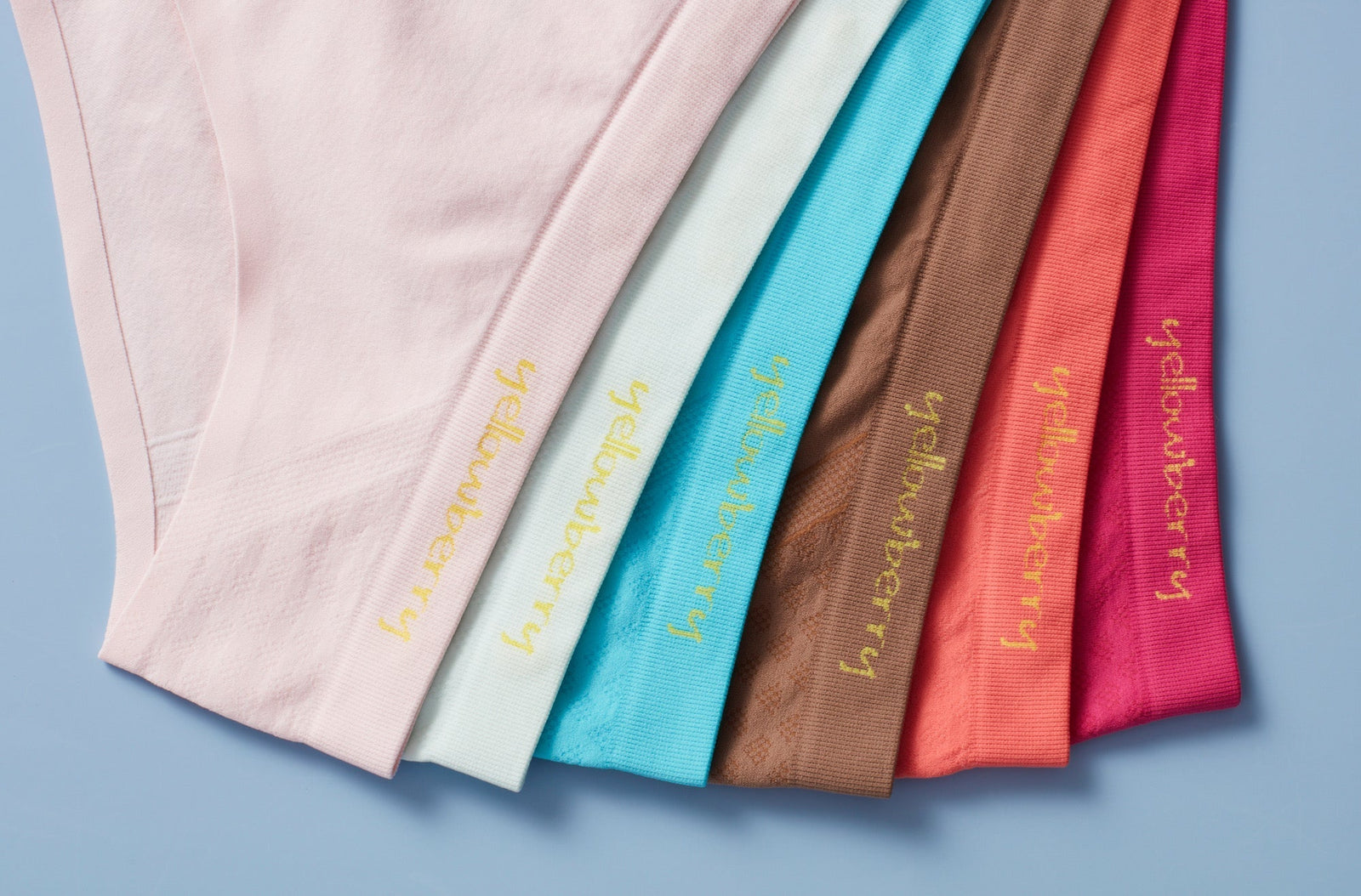 An assortment of Yellowberry Seamless Underwear arranged in rainbow color order on a blue background