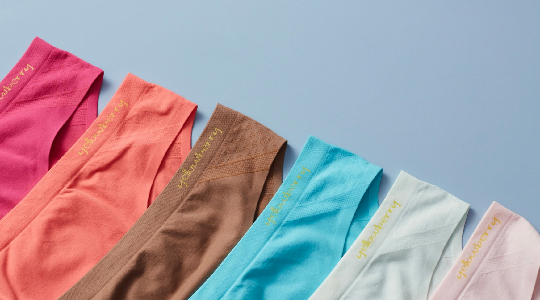An array of Yellowberry Seamless Underwear arranged in order by color of the rainbow on a soft blue background.