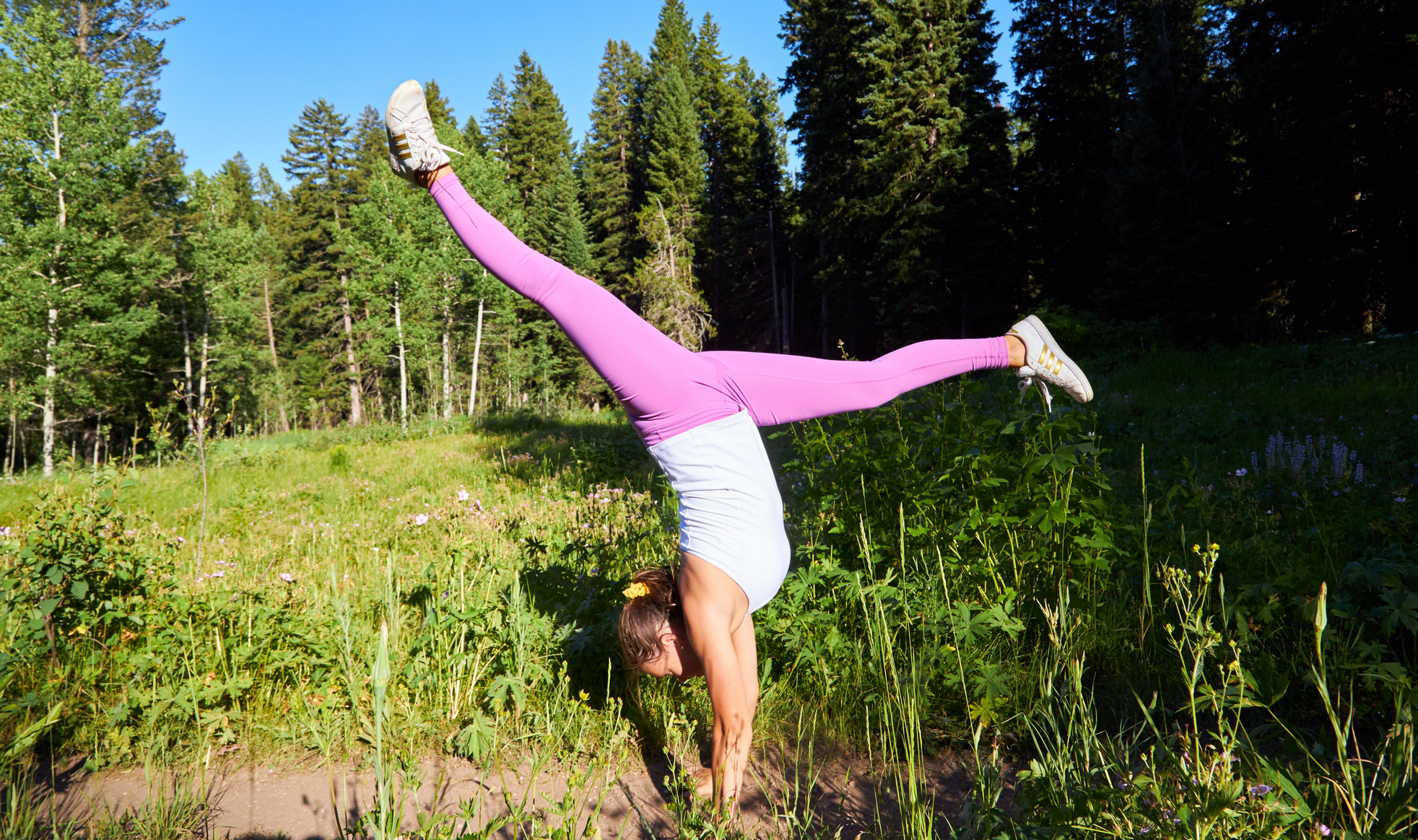 A girl doing a handstand splits in a grassy mountain meadow
