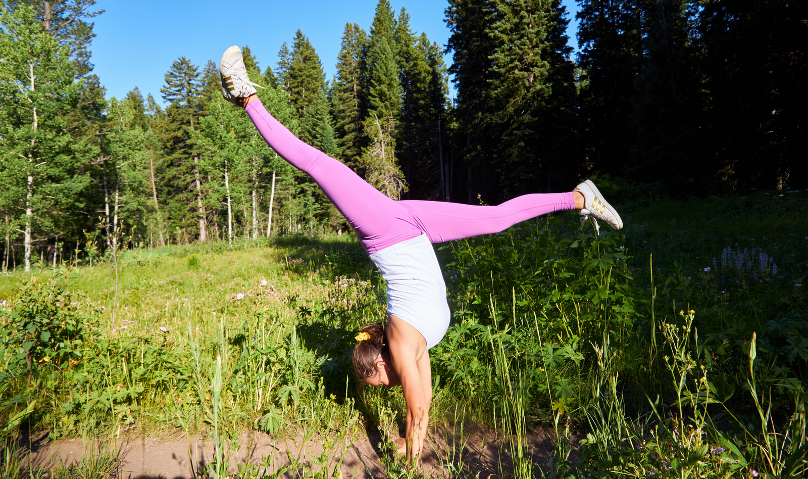 A girl doing a handstand splits in a grassy mountain meadow