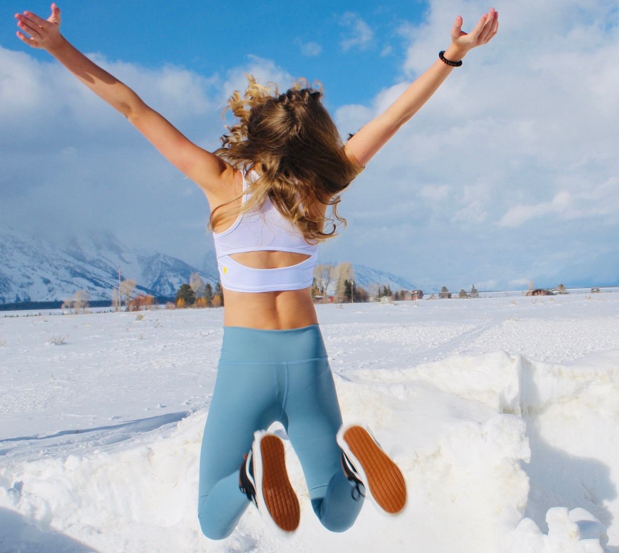 girl jumping in a white yellowberry spors bra against a blue sky and snowbank