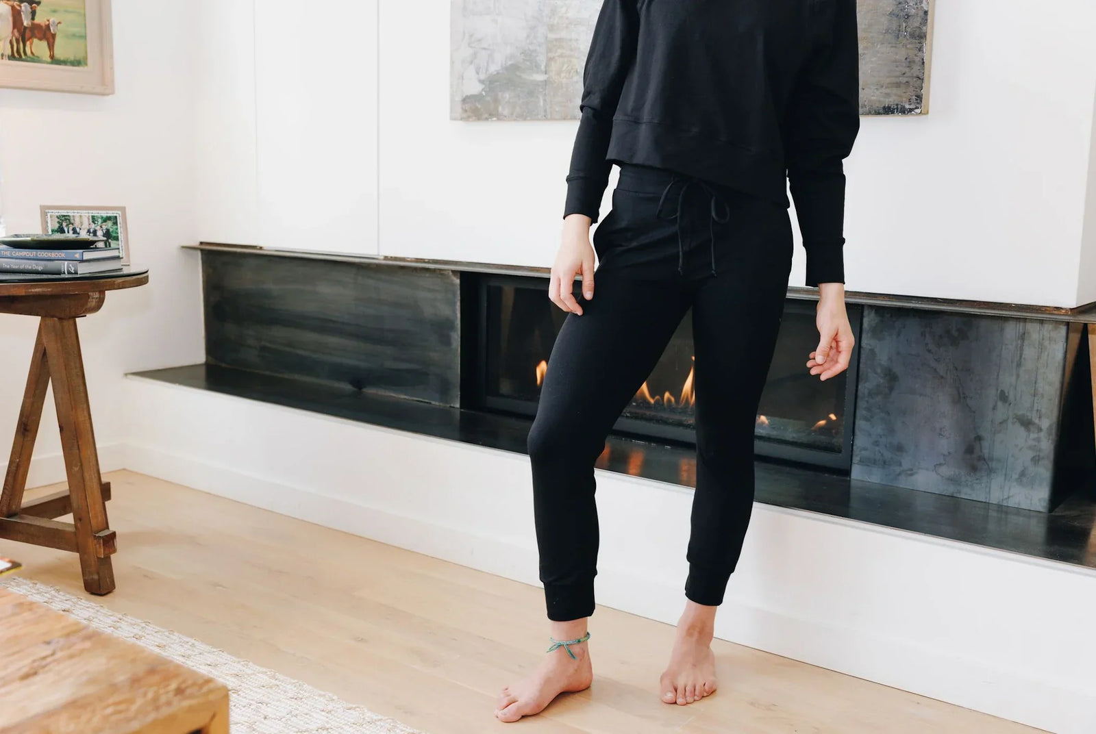 Girl standing in front of a fireplace. She is wearing a black Yellowberry Downtown Hoodie and matching black Yellowberry Uptown Jogger pants.