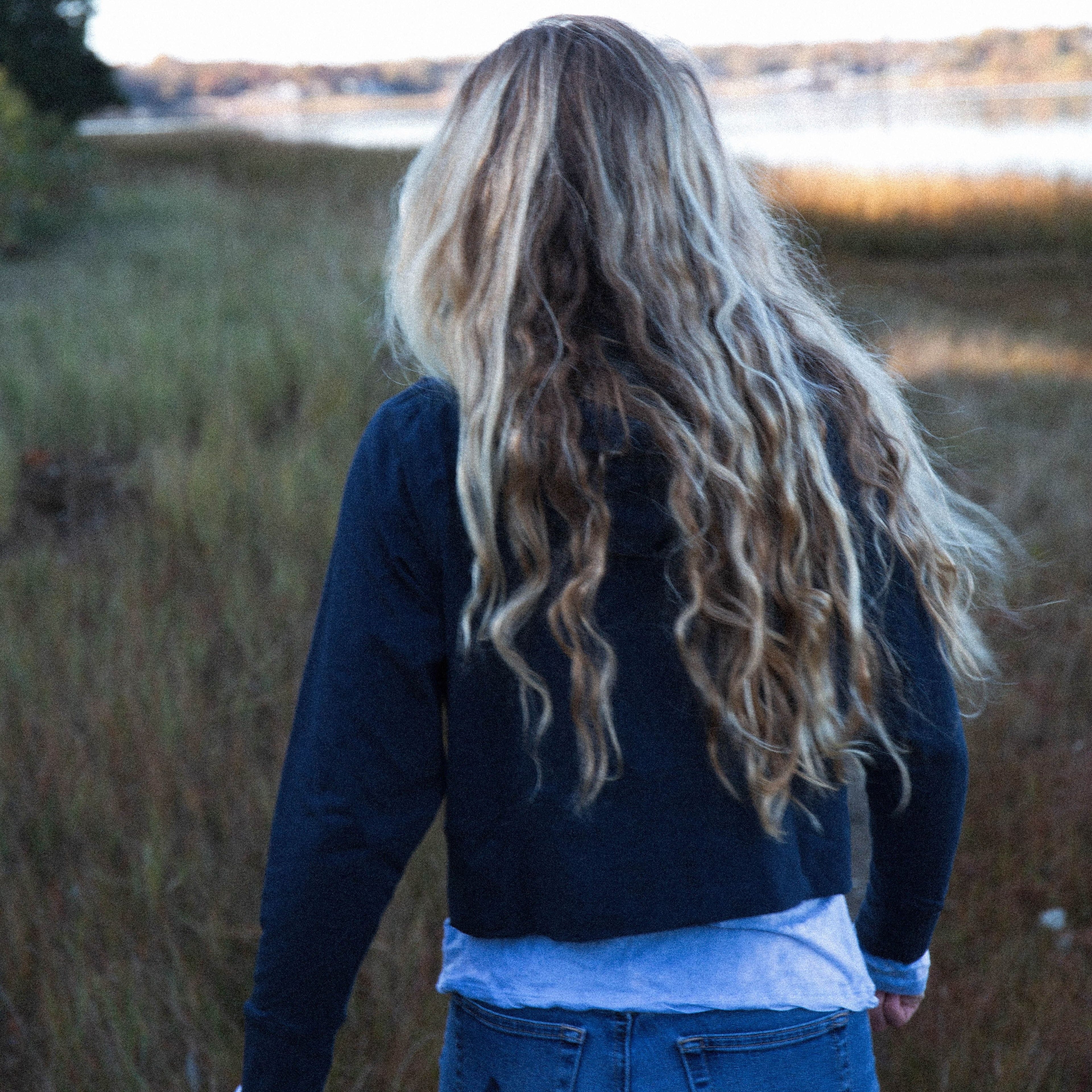 Girl with long blonde hair down her back, walking away from the camera in a meadow