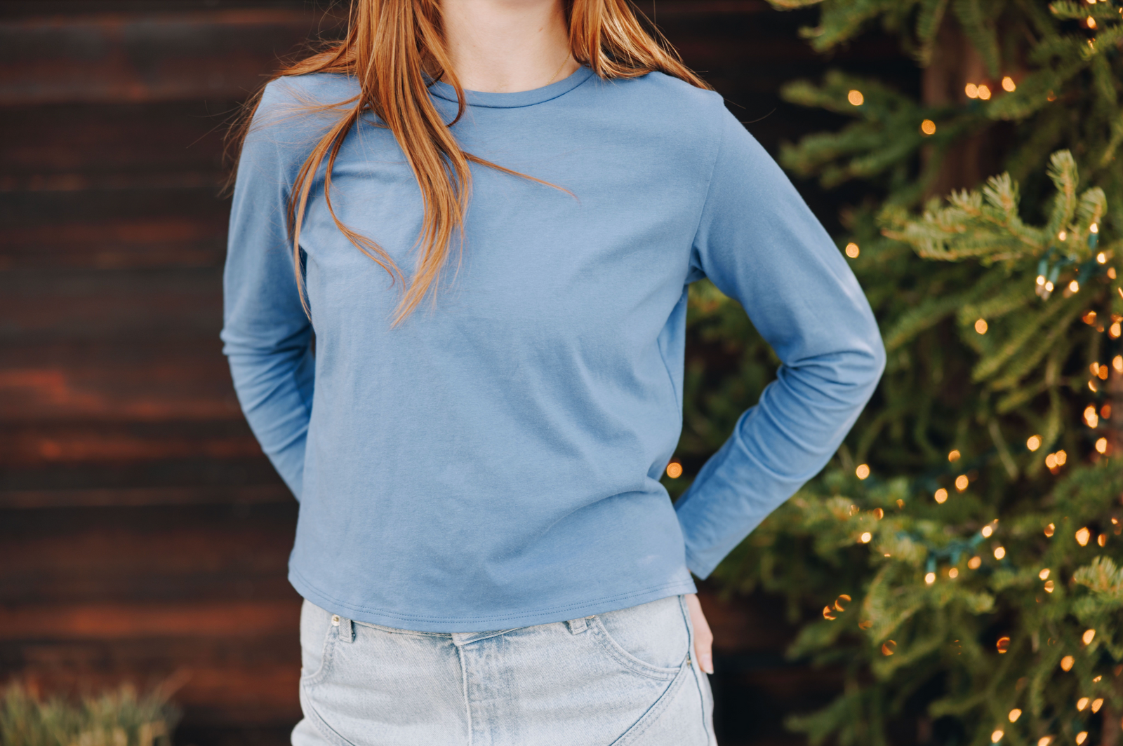 Girl wearing a blue cotton long-sleeve shirt by Yellowberry against a wooden wall