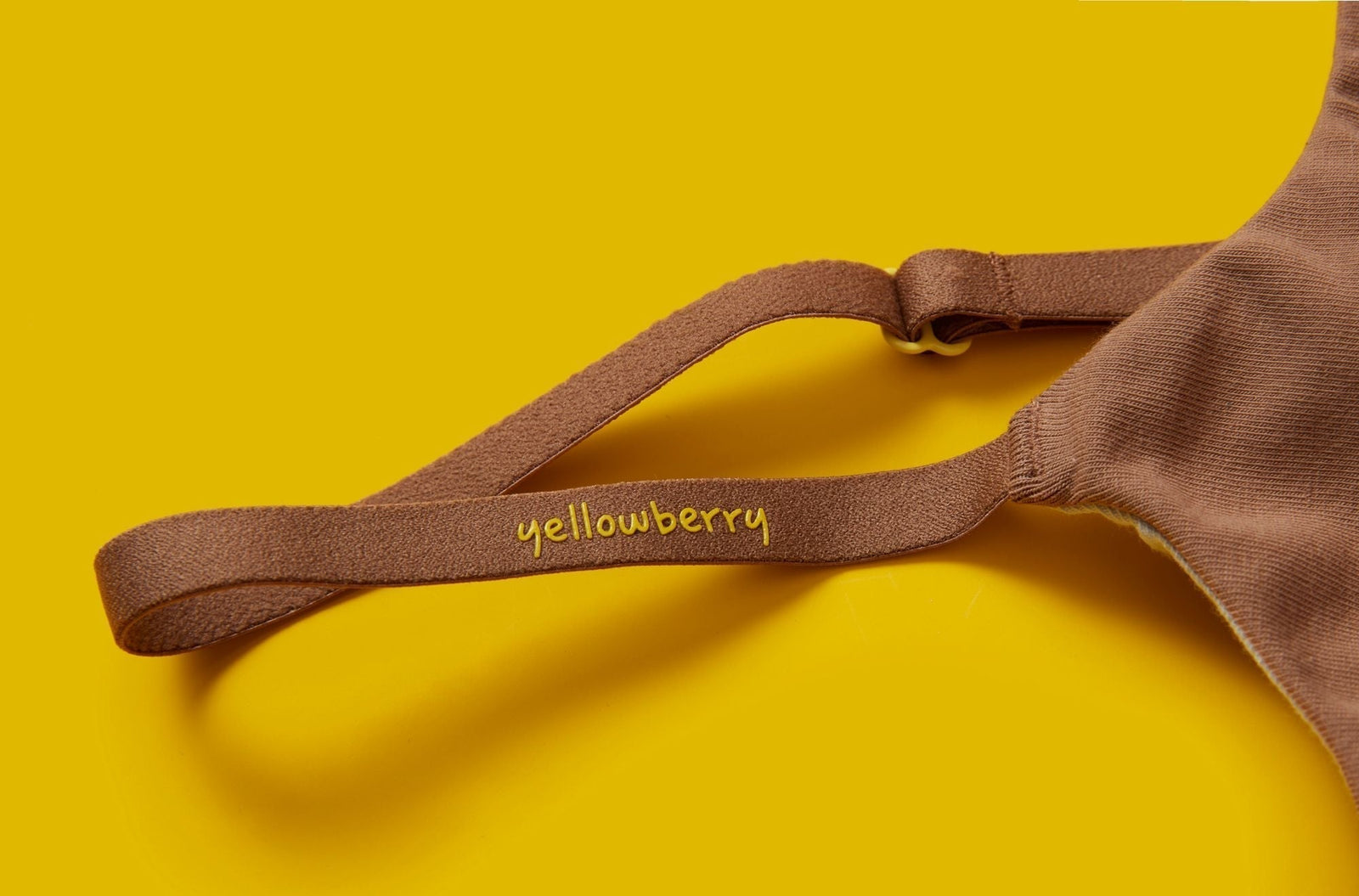 Close up image of a brown bra strap against a yellow background. It is a cotton girls bra with the word "yellowberry" in yellow on the strap