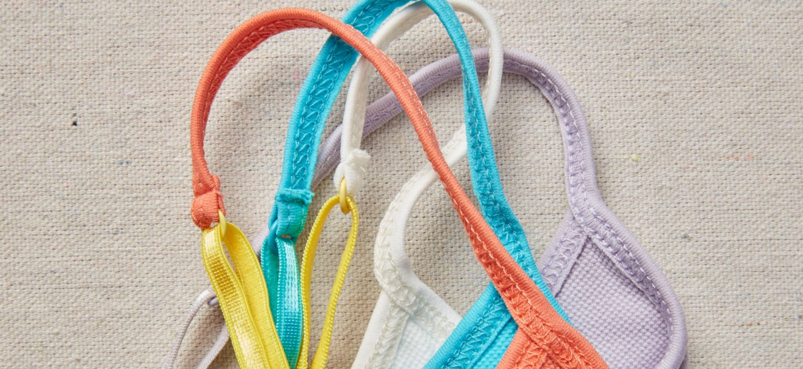 Mutiple bra straps in different colors on top of each other, all on top of a light colored linen brackground