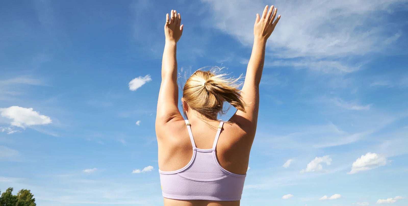 Girl standing against a blue sky. She is wearing a light purple Yellowberry bra and is facing away from the camera.