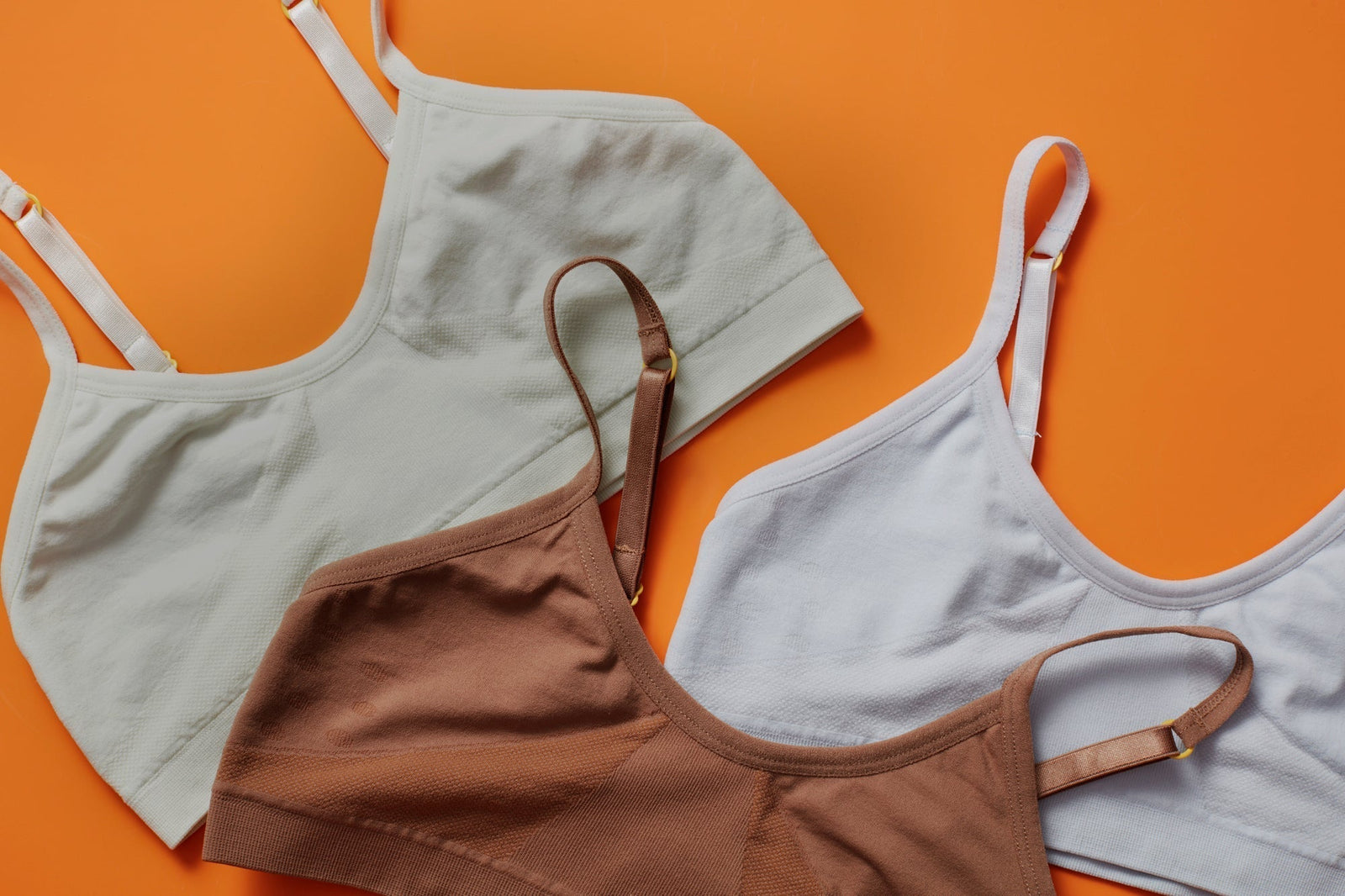 Three Yellowberry seamless bras laying on an orange background. Three colors, one mocha, one beaach glass, and one raindrop all arranged on the background.