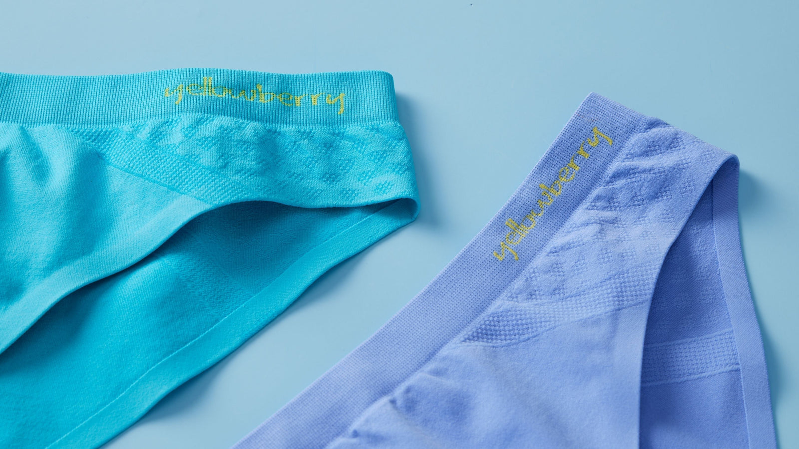 Two pair of Yellowberry's seamless underwear, one in ocean color and one in wave color, are laying on a dull blue background. They word "yellowberry" is embroidered in yellow on each pair.
