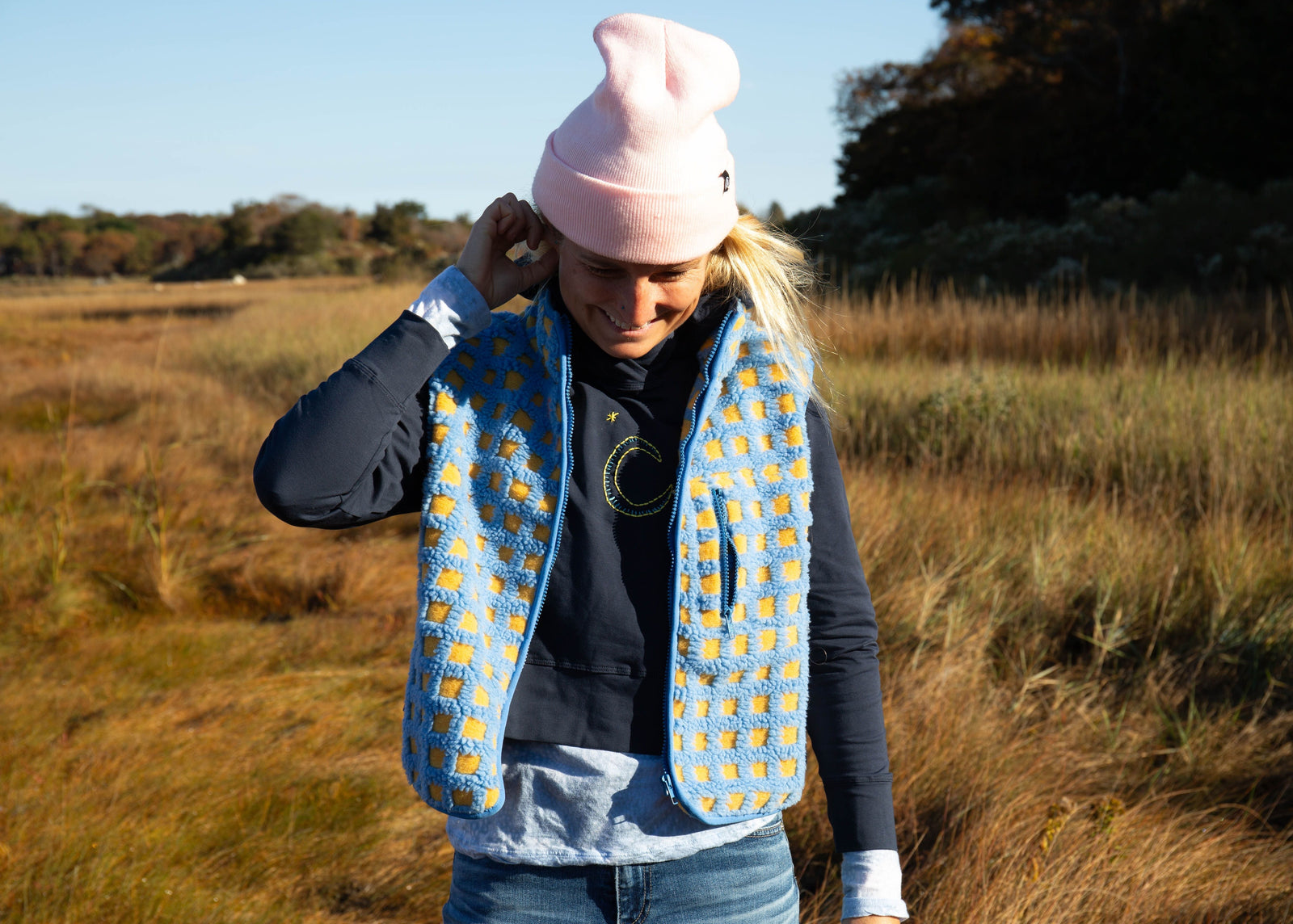 Girl wearing a Yellowberry hoodie. She is standing outside and has it styled with a blue vet and cute pink hat.