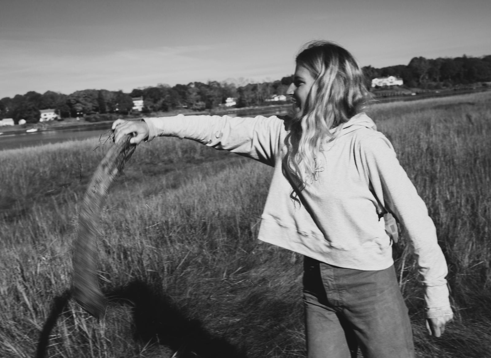 Black and white image of girl in a Yellowberry hoodie, tossing a piece of wood.