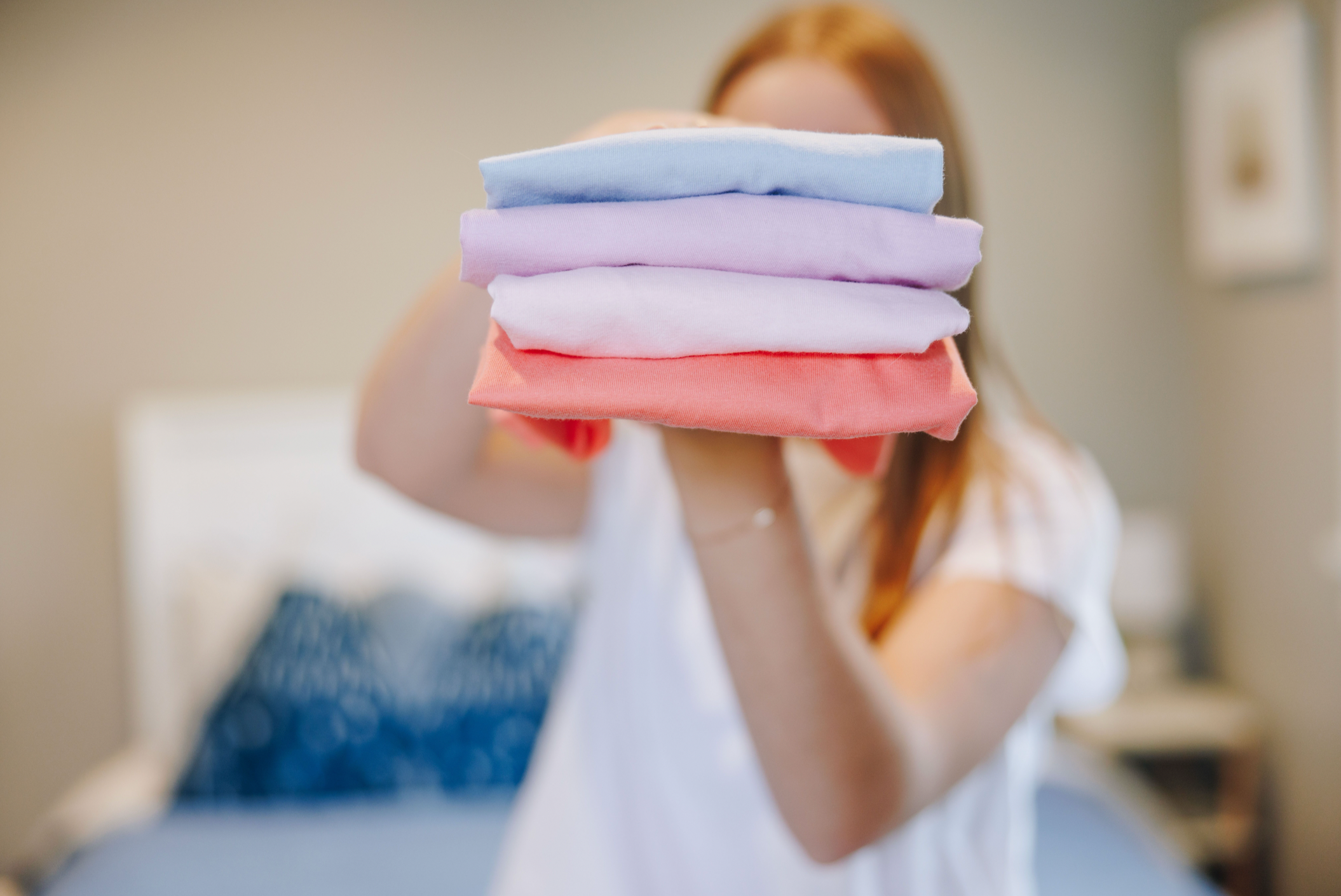 Girl holding a stack of folded cotton t-shirts by Yellowberry