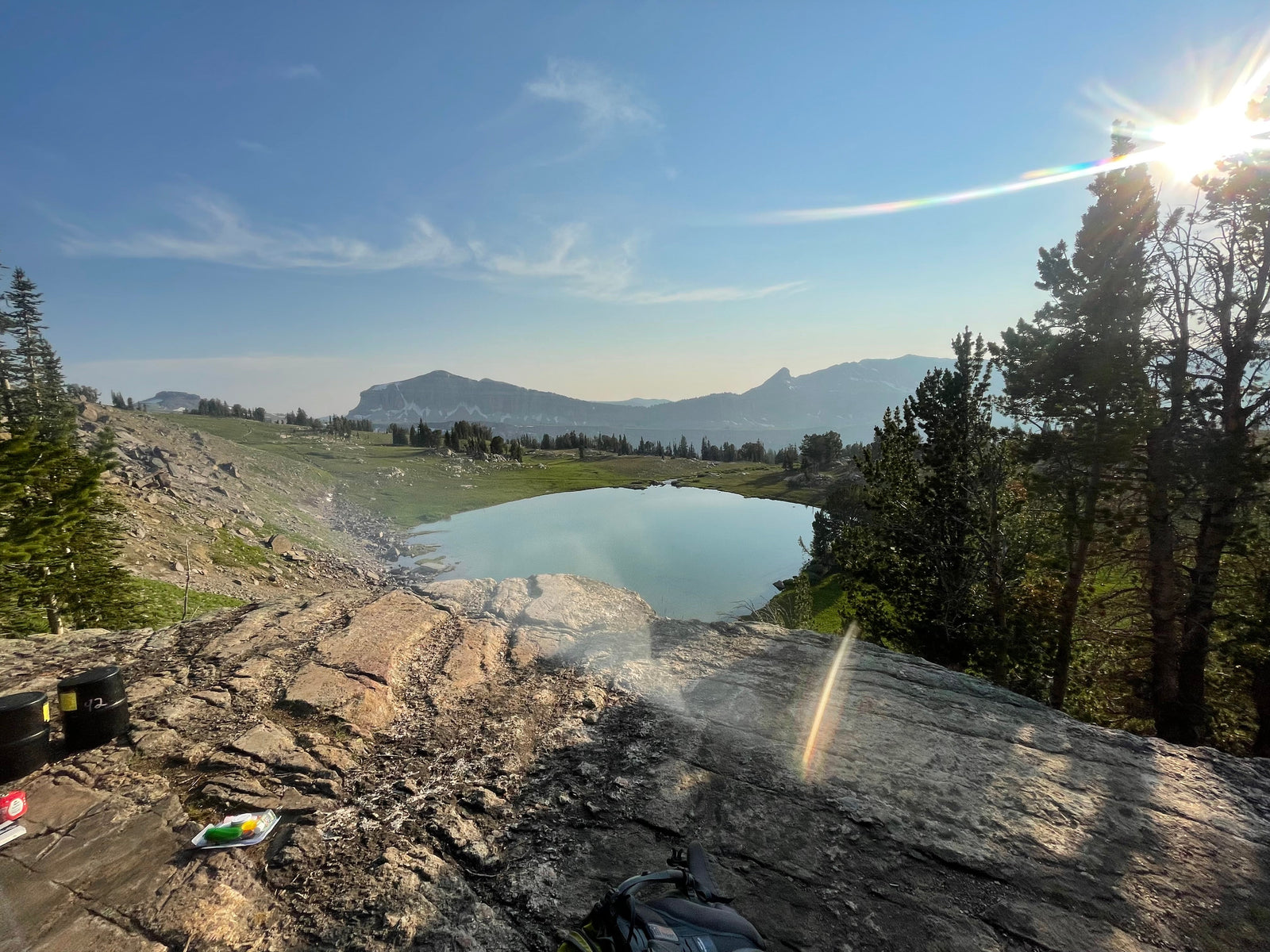 A beautiful view of a rocky ledge overlooking a bllue lake. It is an outdoor camping spot.