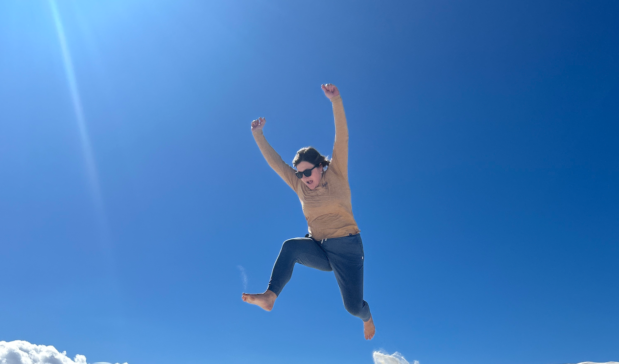 Girl jumping against a bright blue sky. Her hands are in the air and she is smiling