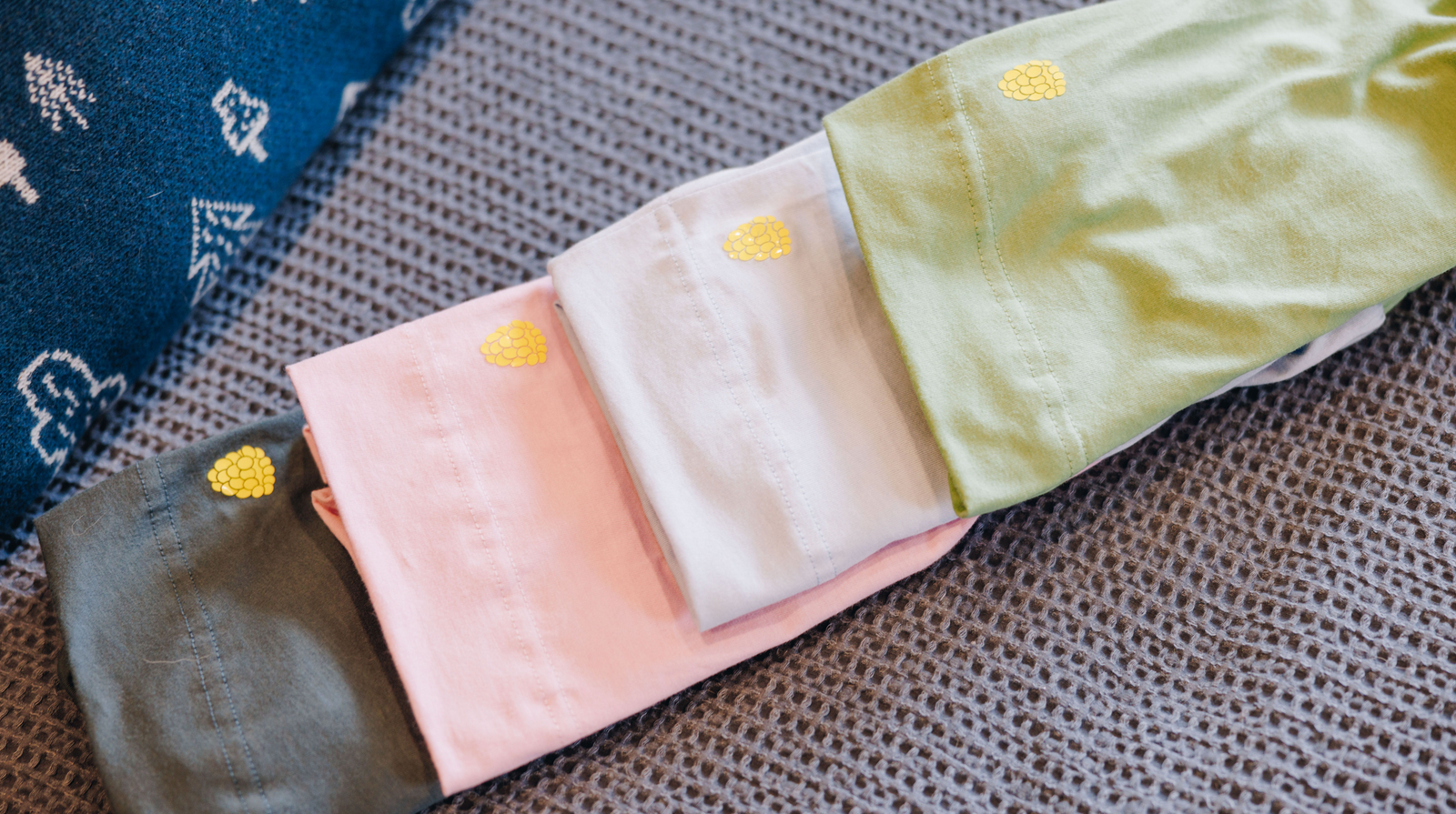 Four pairs of different colored girls cotton shorts laid out on a patterned background, each pair folded in half with a Yellowberry logo on the back 