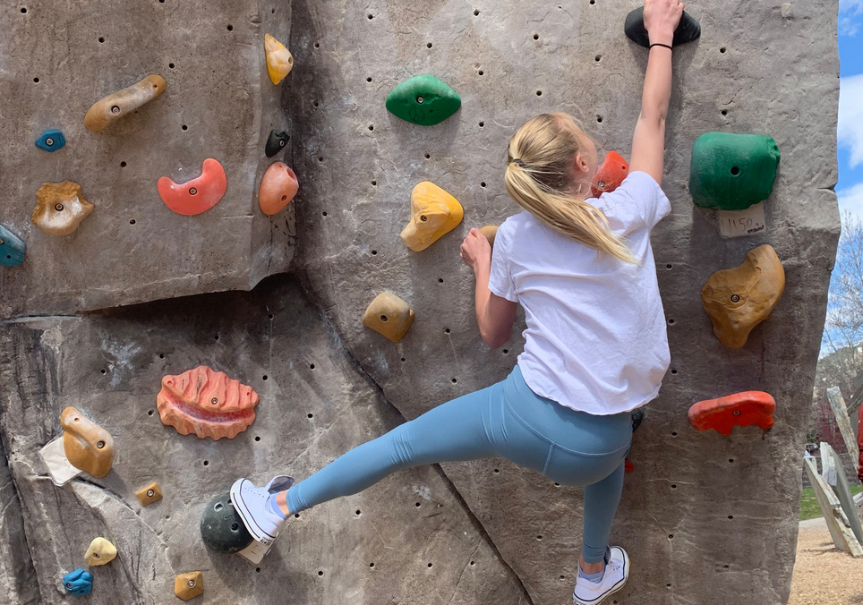 Girl on a climbing wall wearing a flowy white t-shirt and blueish grey colored leggings