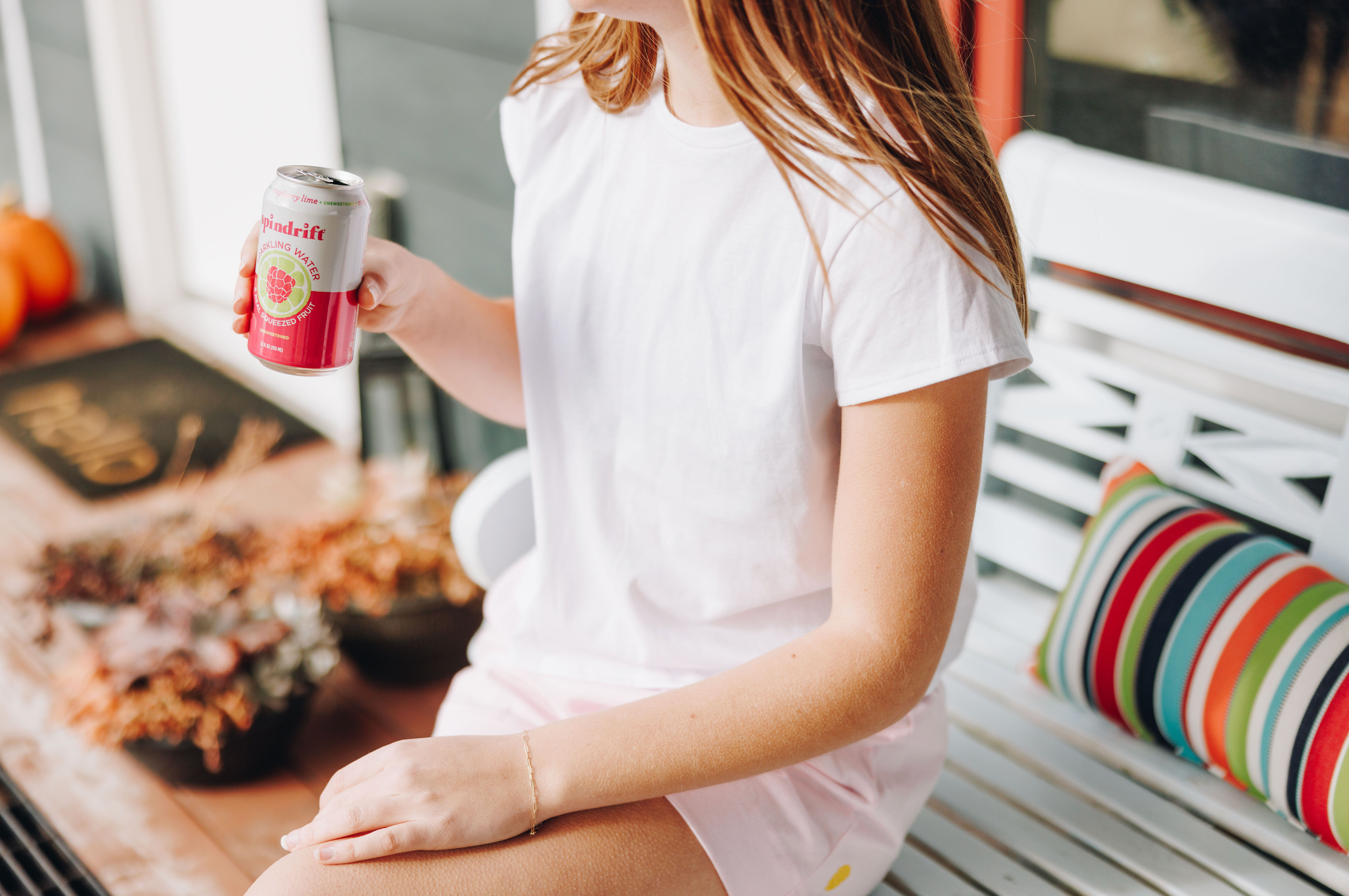 Girl sitting down on a bench in a white cotton t-shirt and pink shorts holding a drink in her hand.
