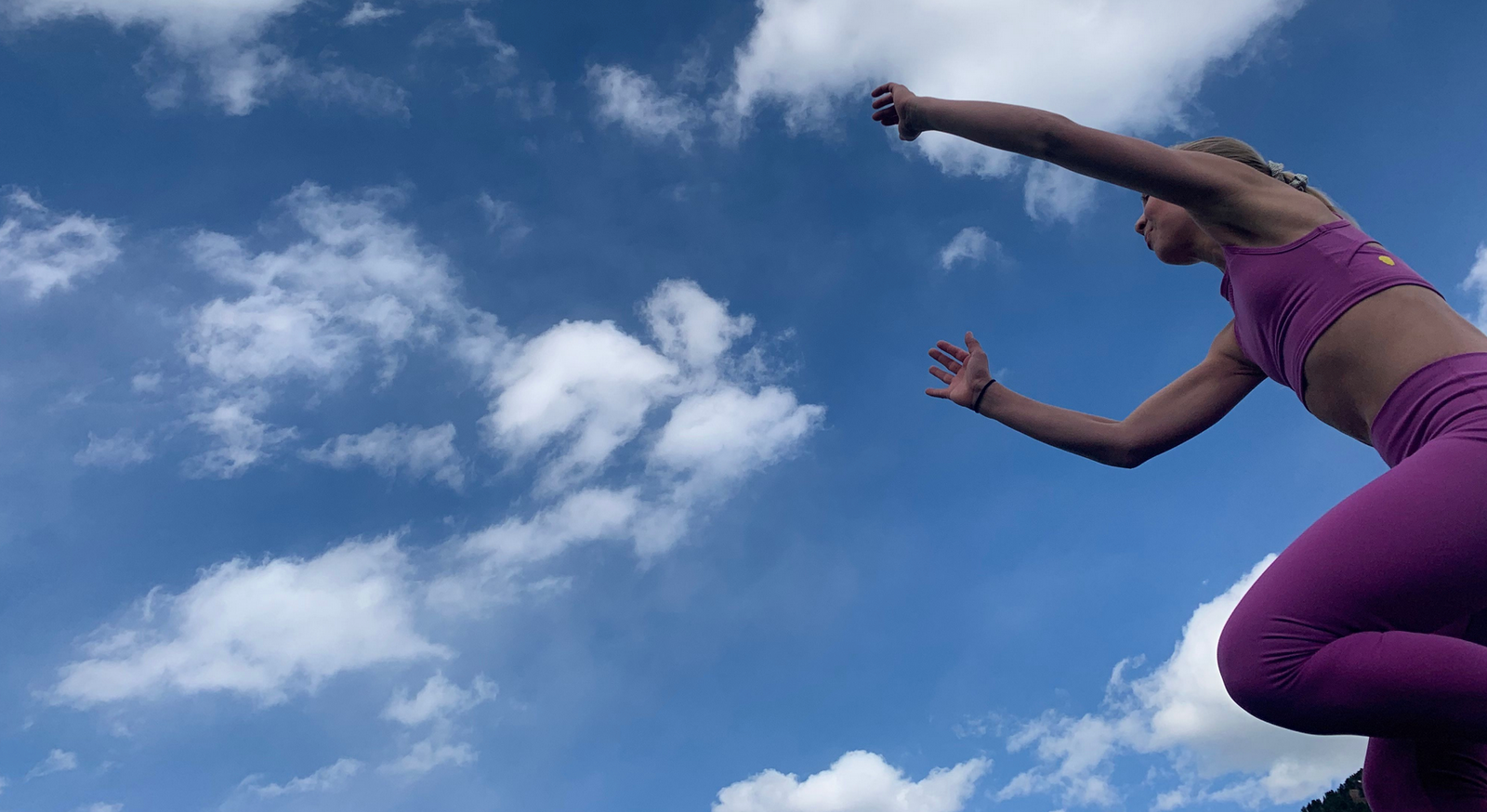 Girl wearing matching purple crop tops and leggings jumping in front of a blue sky