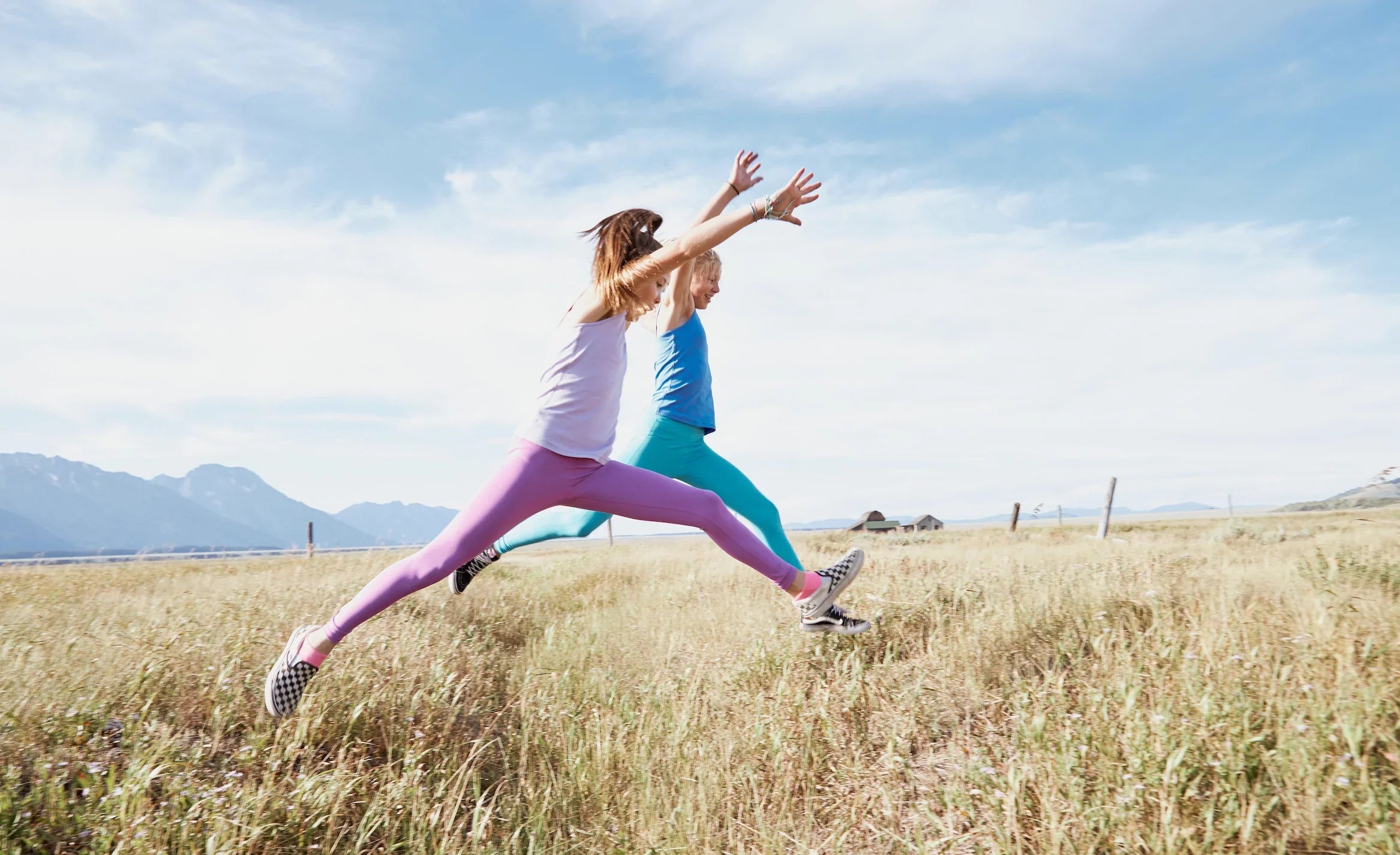 Two girls in camisoles jumping over high grass