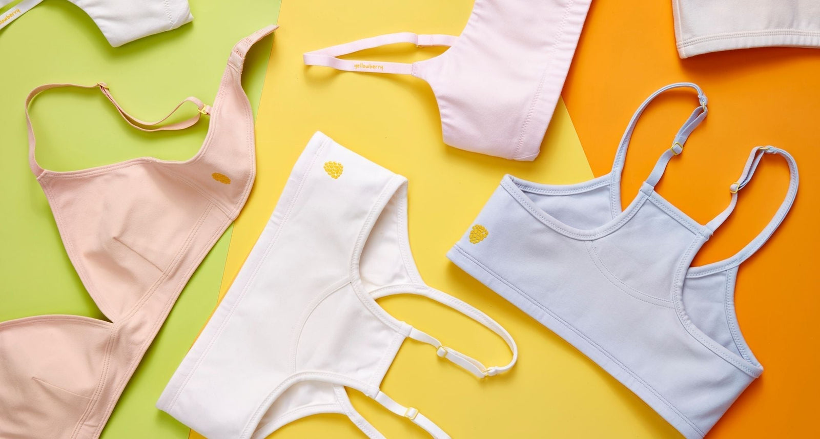 An assortment of basic colored Yellowberry Bras displated on a multi colored background of orange, yellow, and green.