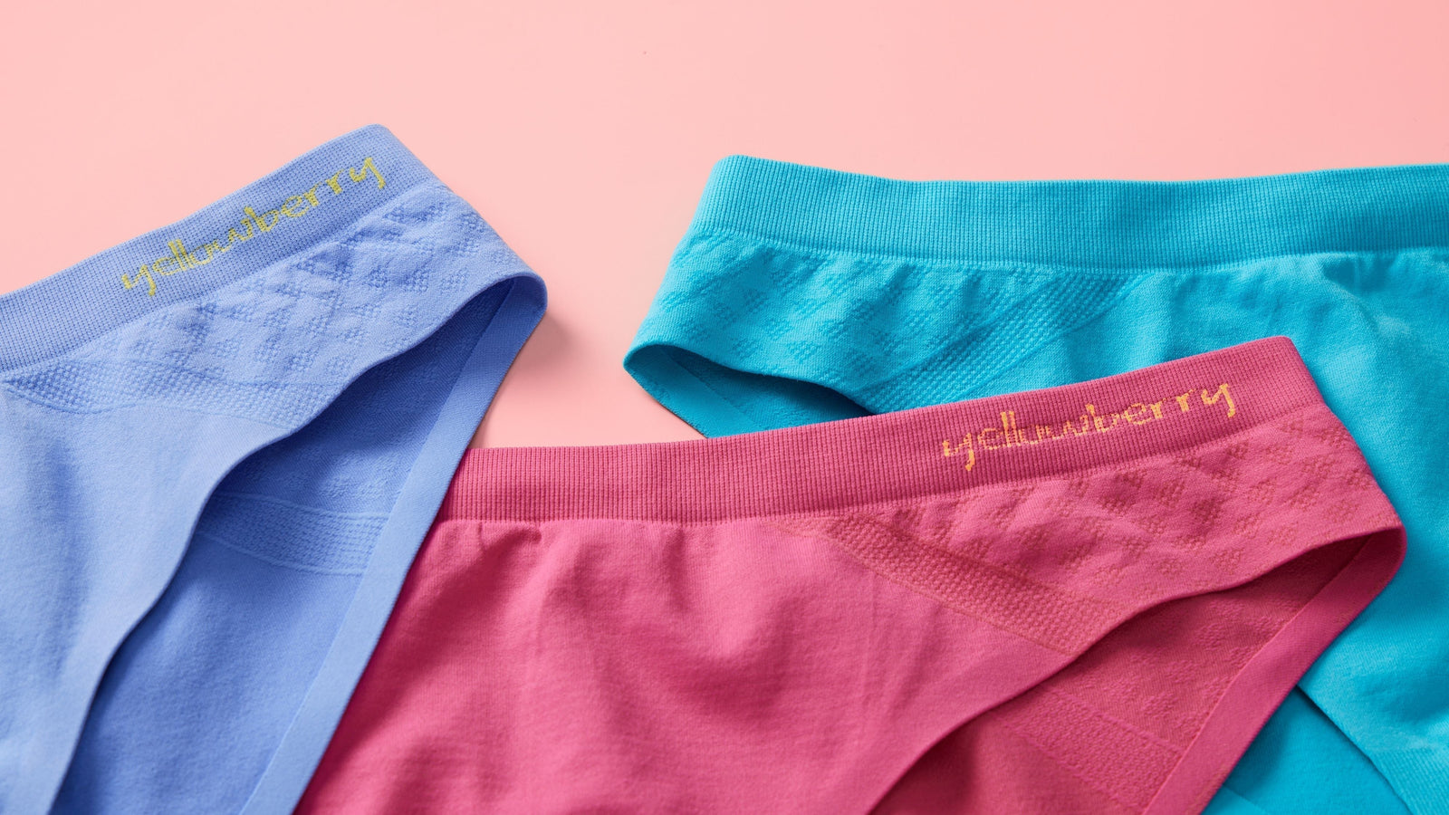 Three pairs of Yellowberry seamless underwear on a pink background. One is watermelon color, one is ocean color, and the other is wave color.