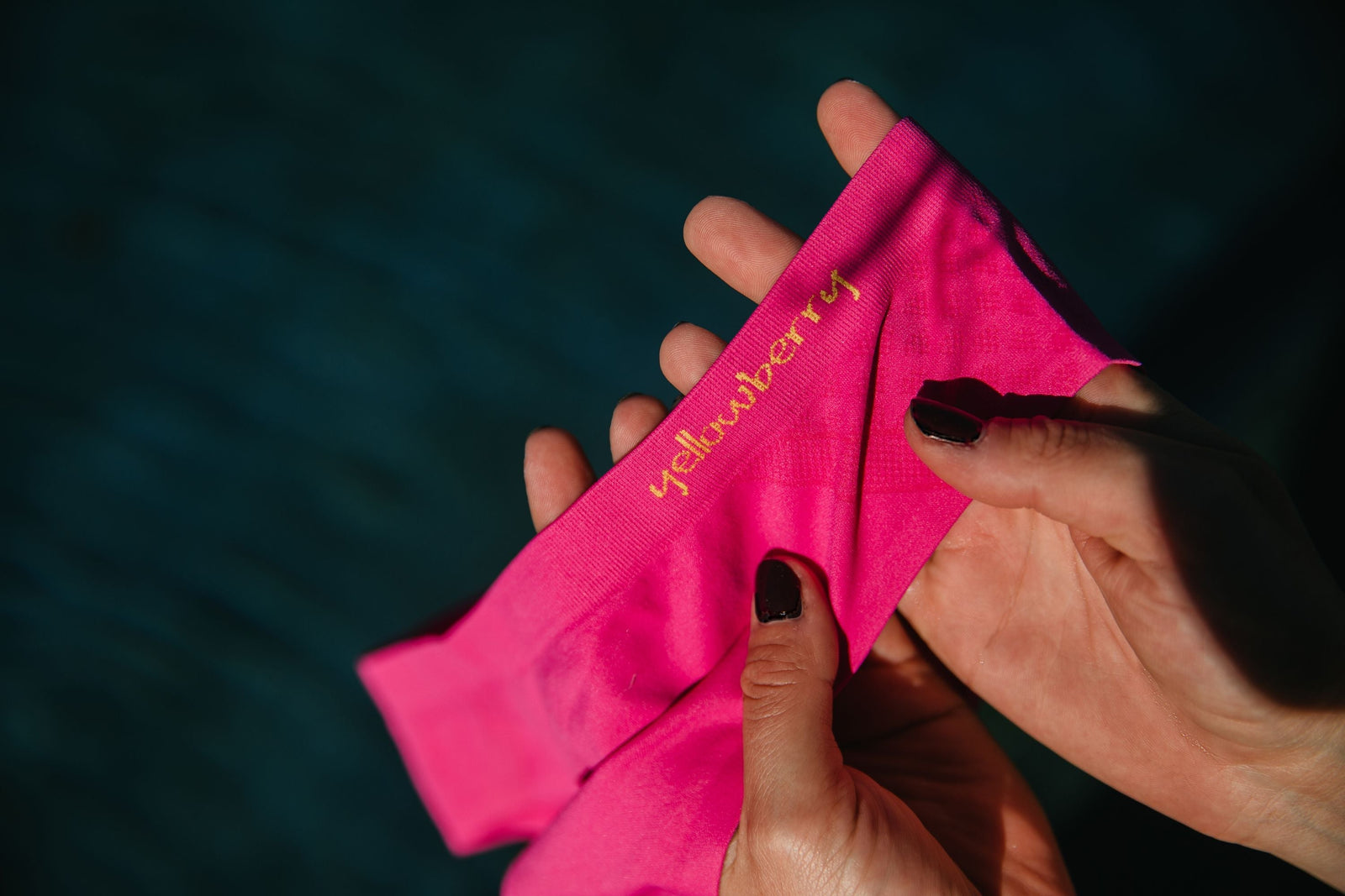 A close-up image of a pair of watermelon pink Yellowerry Seamless Underwear. They are held in someones hands with the Yellowberry word embroidered prominently. 