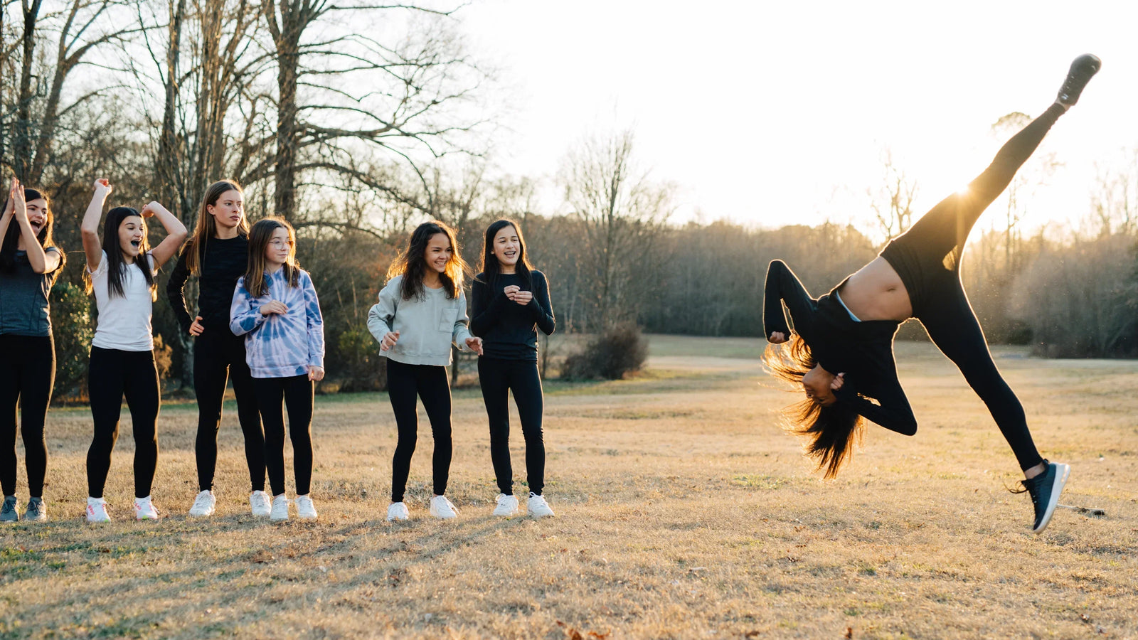 A girl doing a flip in front of her friends who cheer her on!