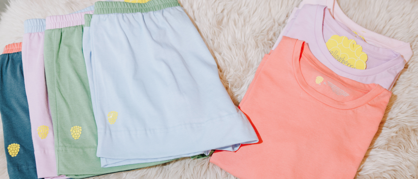 Four pairs of multiple colored cotton shorts folded and laid out with three cotton tshirts, also laid out and folded. Everything is laying on a soft blanket.