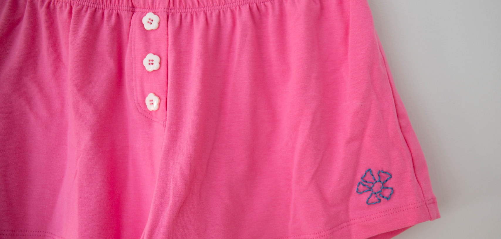 Pink cotton shorts with a blue embroidered flower and three white buttons