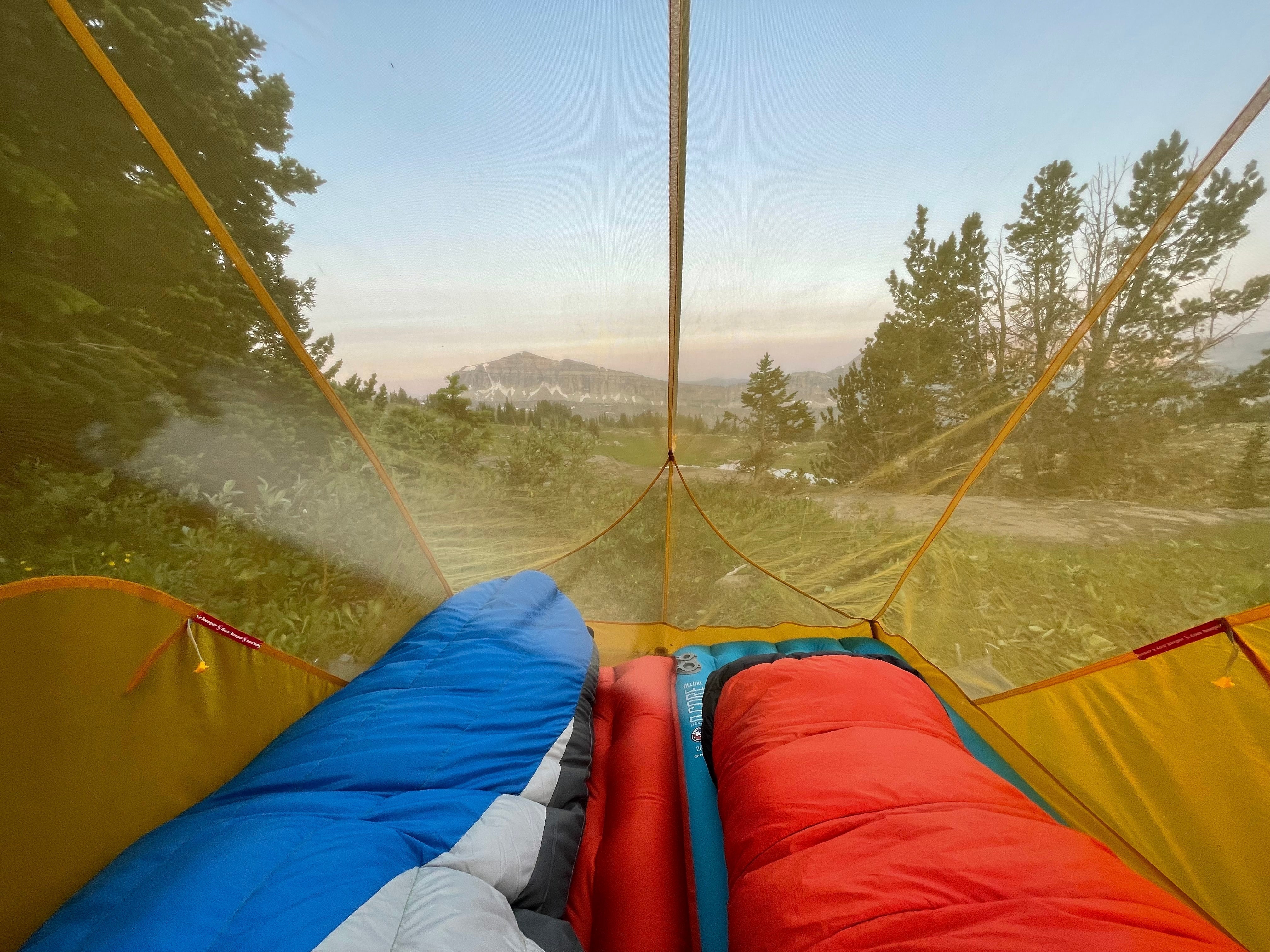 Two sleeping bags in a tent with a view of the snow capped mountains behind them. 