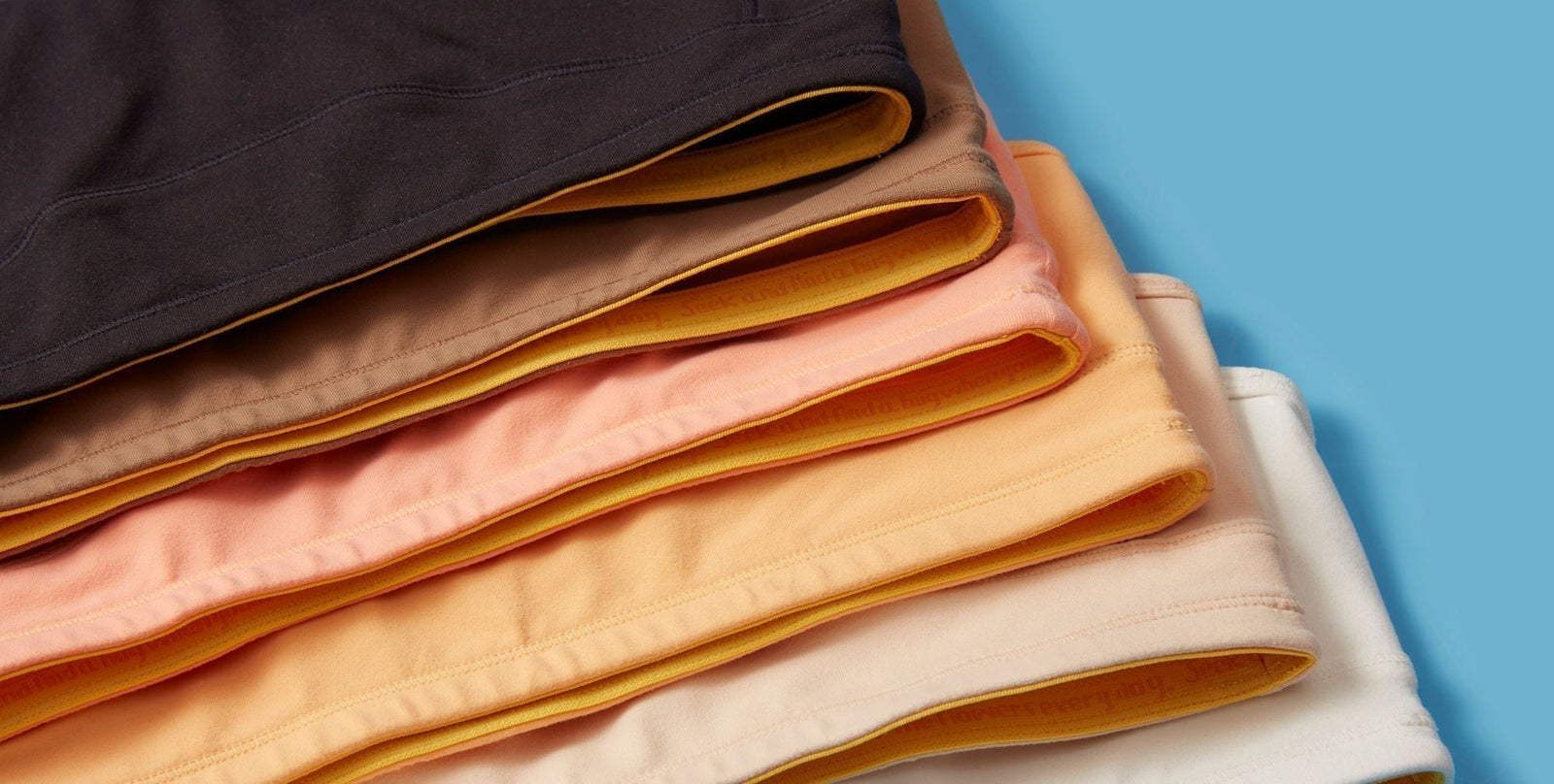 Close-up image of multiple colors of the Yellowberry Tink Bra. They are styled together with complementary color order on a blue background