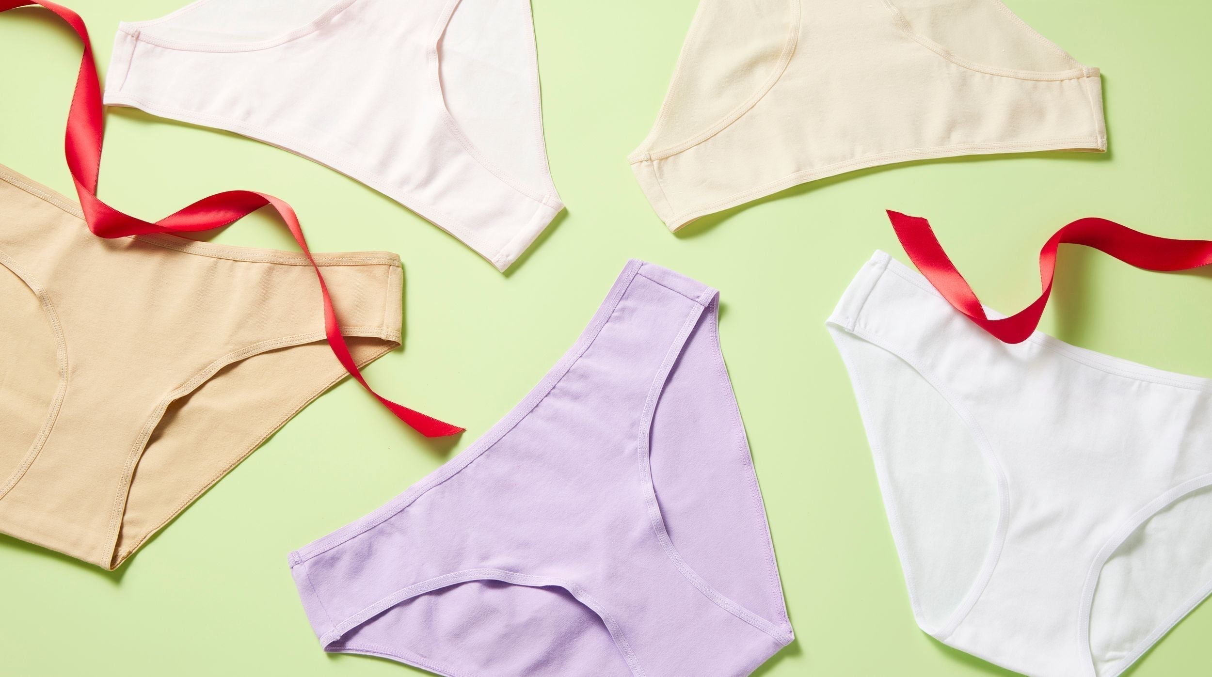 Multiple pairs of girls cotton underwear styled on a light green background with a bright red holiday ribbon laying on top