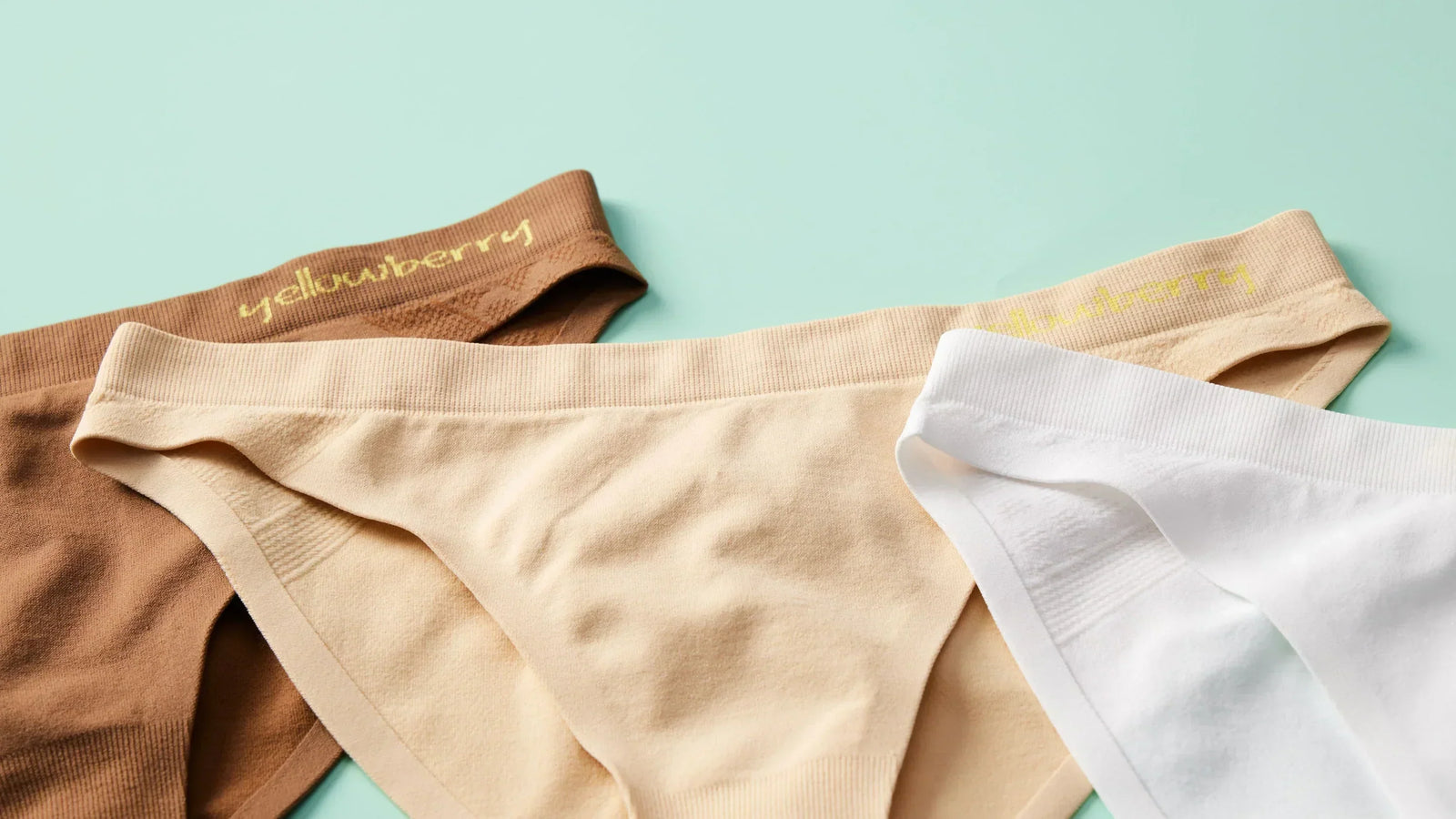 Three pair of Yellowberry seamless underwear. One is mocha colored, one is beige colored, and the third is white colored. They are on a light green background.