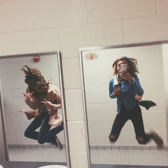 Two girls jumping up for a photo in front of a sink and mirror in the bacthroom