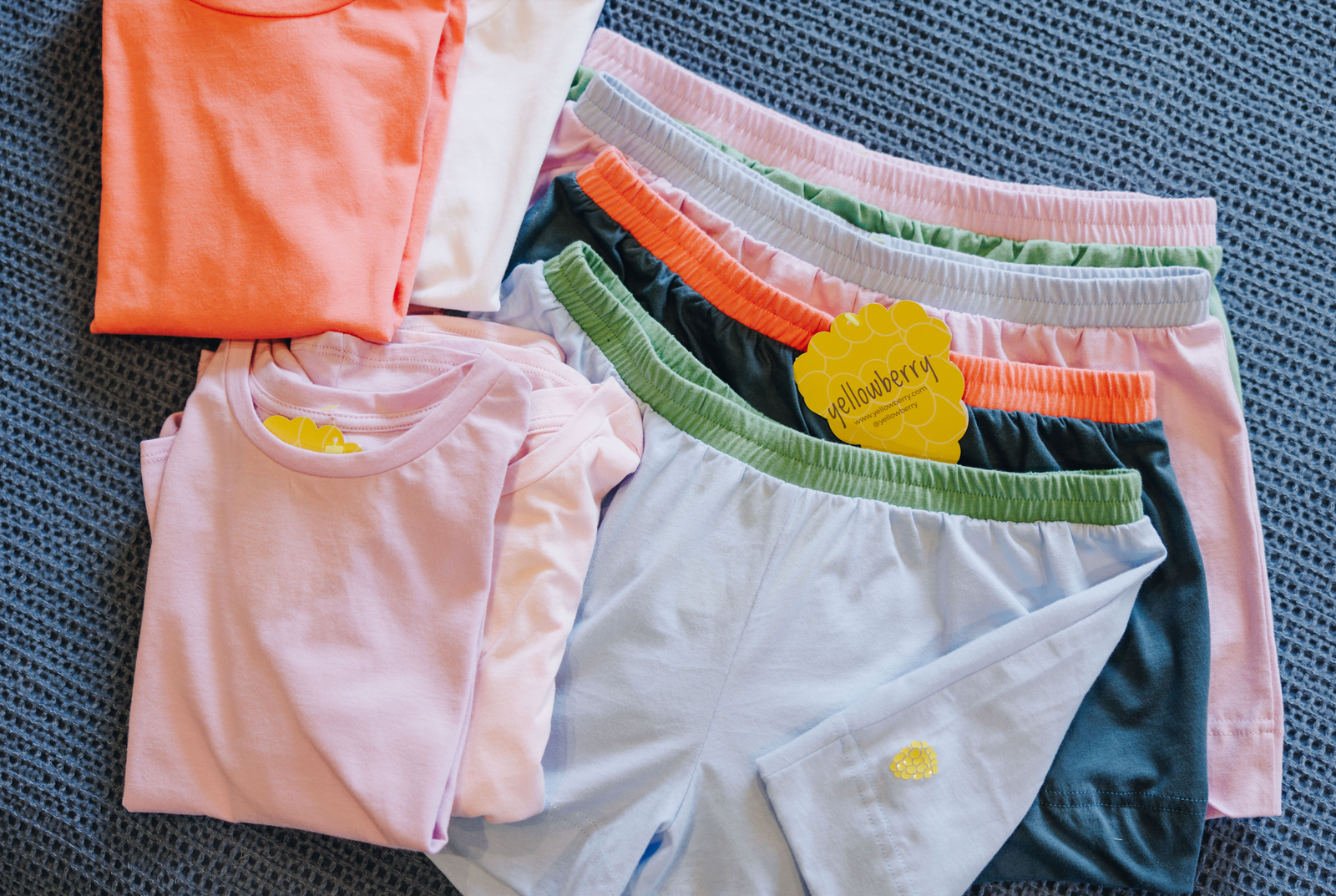 An assortment of folded cotton t-shirts and cotton shorts laying on a blue background