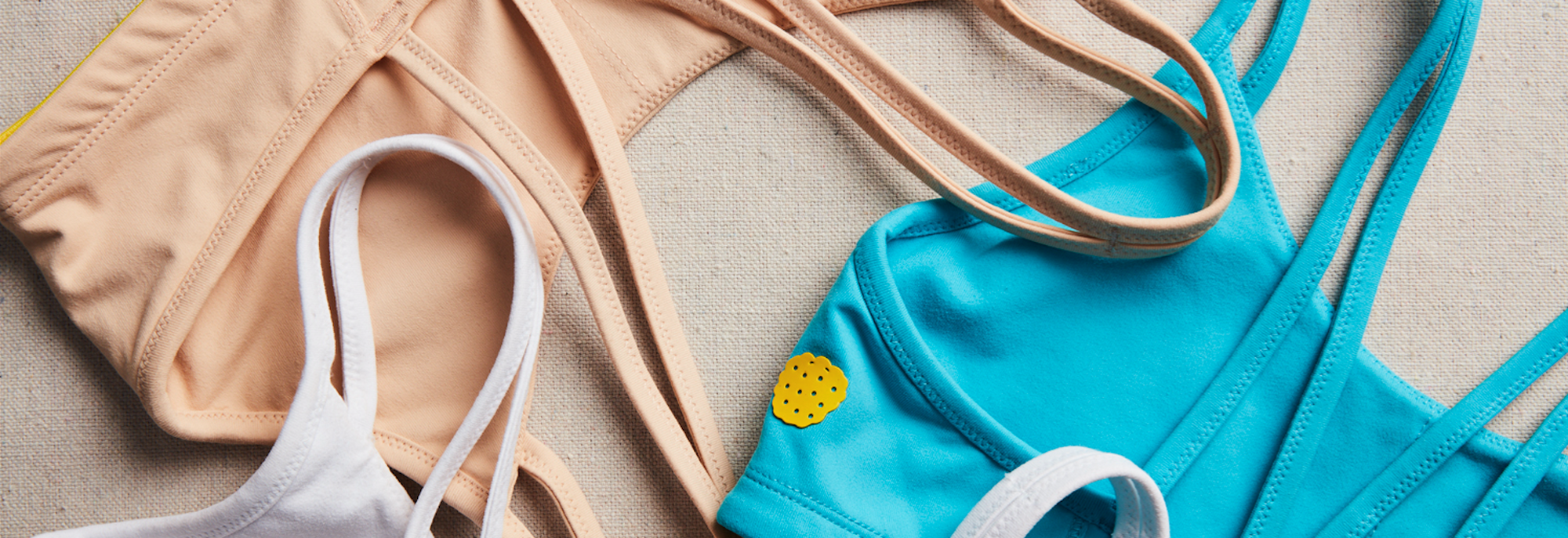 Detail shot of three Yellowberry Hybrid Sports Bras. Each one made with full coverage support, double layered antimicrobial fabrics, and all-day comfort.