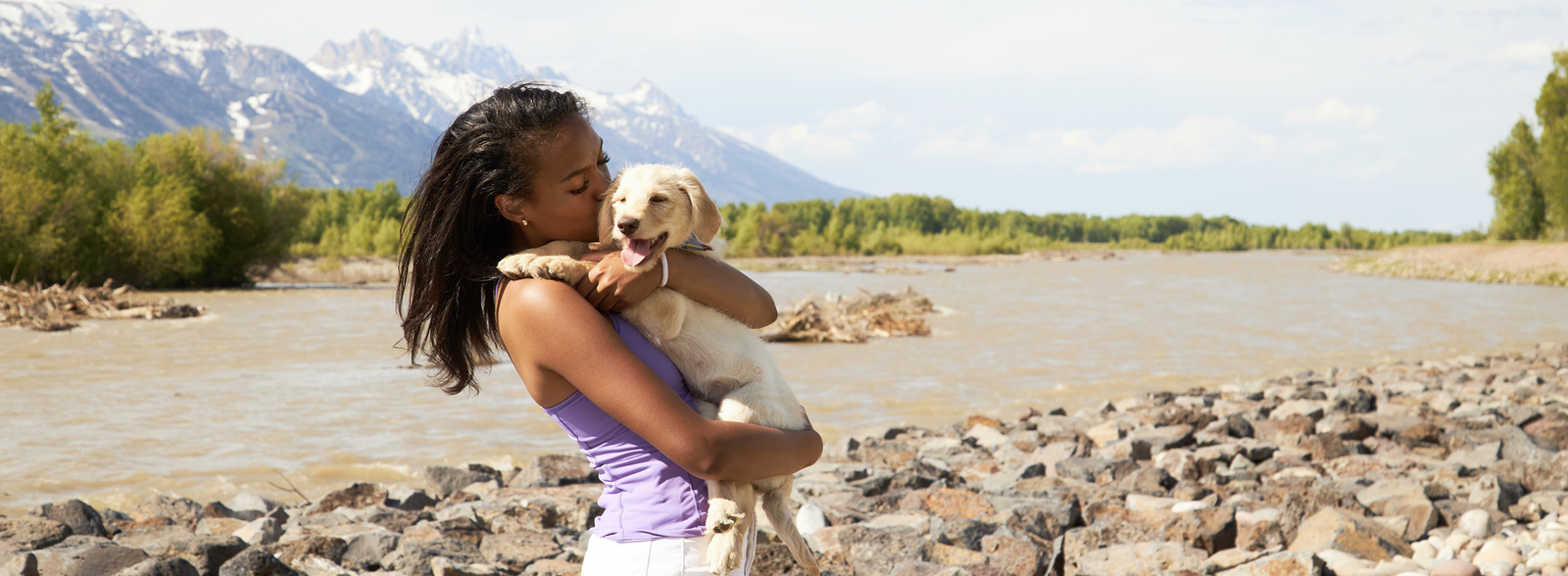 Girl holding and kissing her puppy while standing in front of a river