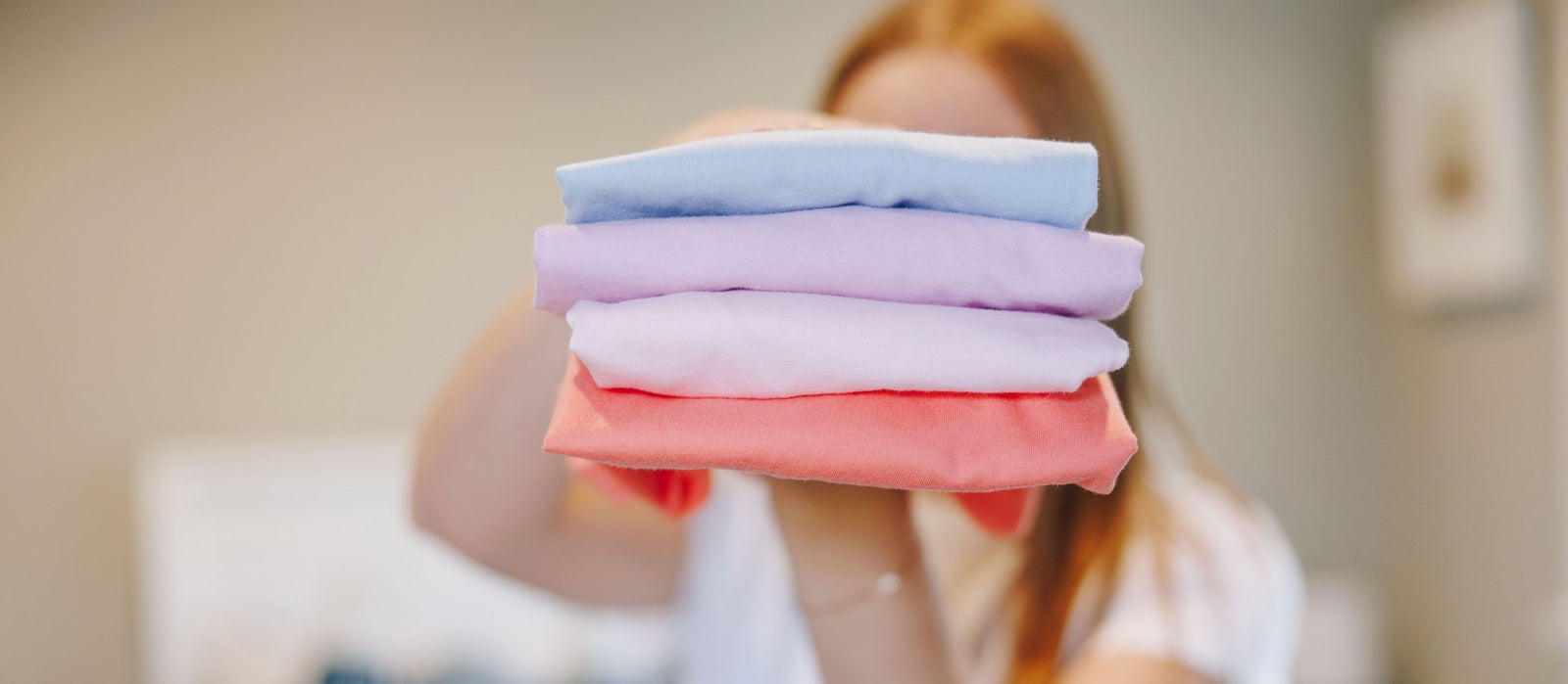 Girl holding a stack of folded, colorful cotton t-shirts 