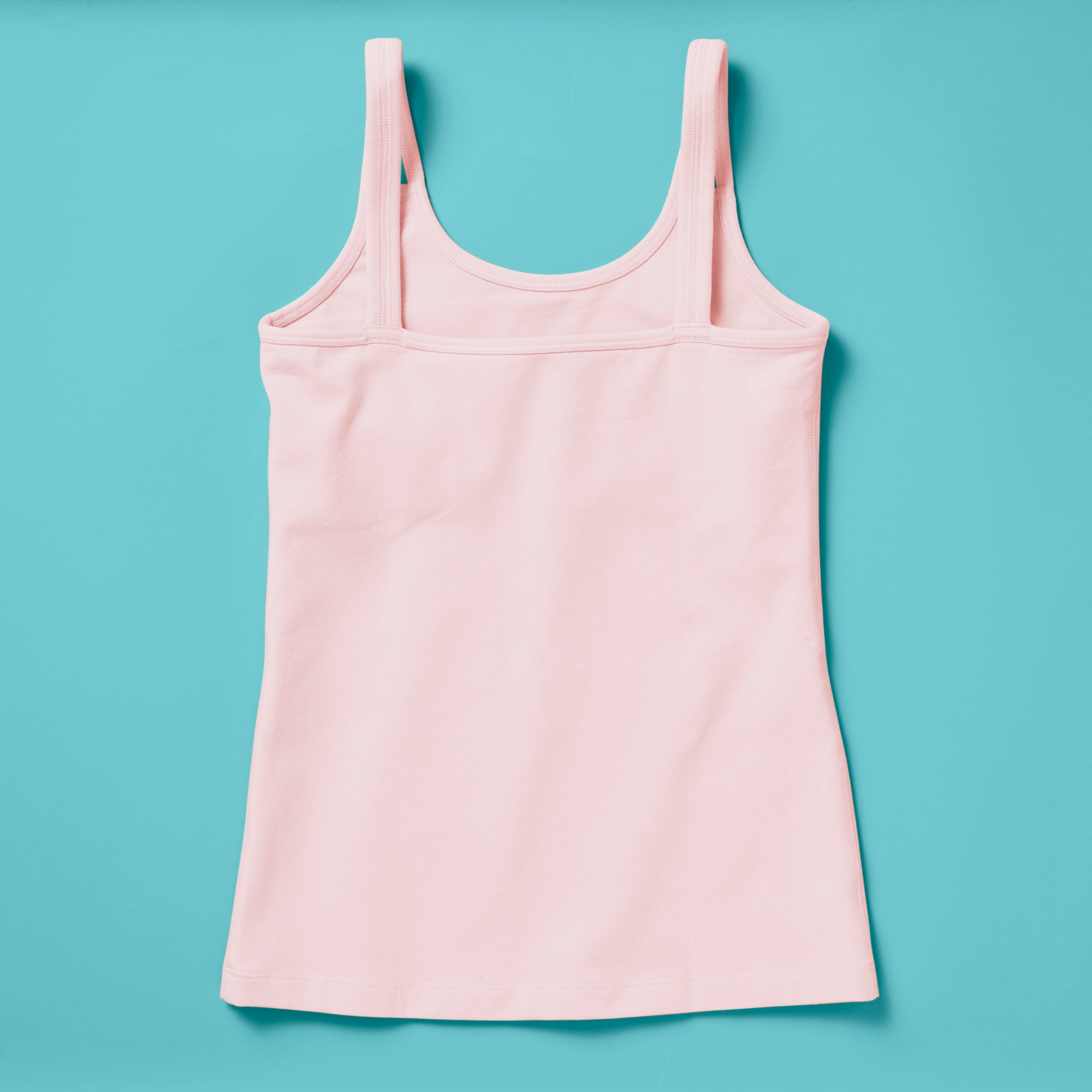 Laydown image of a light pink girls cotton tank top with a shelf bra on an aqua background, back