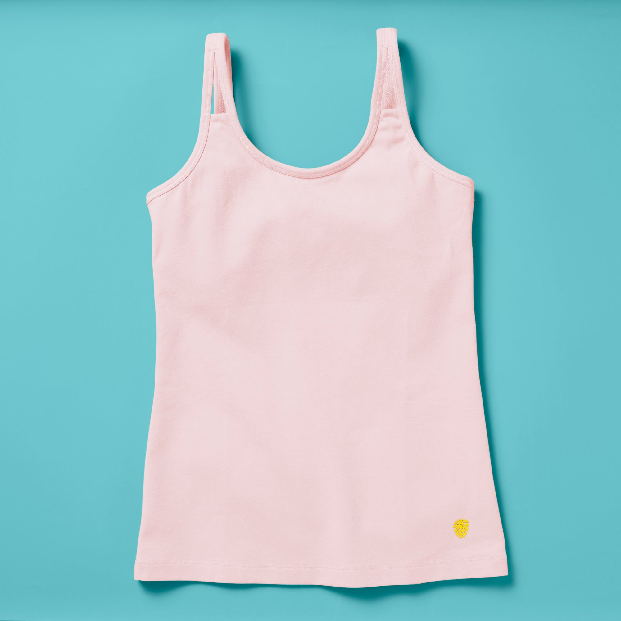 Laydown image of a light pink girls cotton tank top with a shelf bra on an aqua background, front