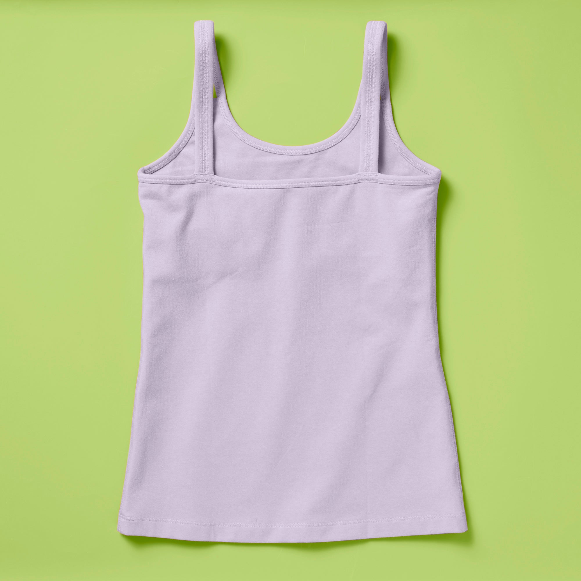 Laydown image of a light purple girls cotton tank top with a shelf bra on a soft green background, back