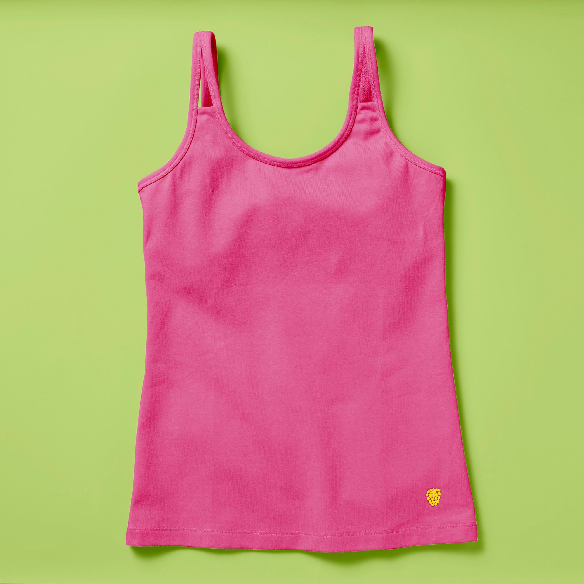Laydown image of a hot pink girls cotton tank top with a shelf bra on a soft green background, front
