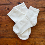 Three pairs of white ribbed ankle socks arranged on a rustic brown wooden surface.
