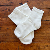 Three pairs of white ribbed ankle socks arranged on a rustic brown wooden surface.