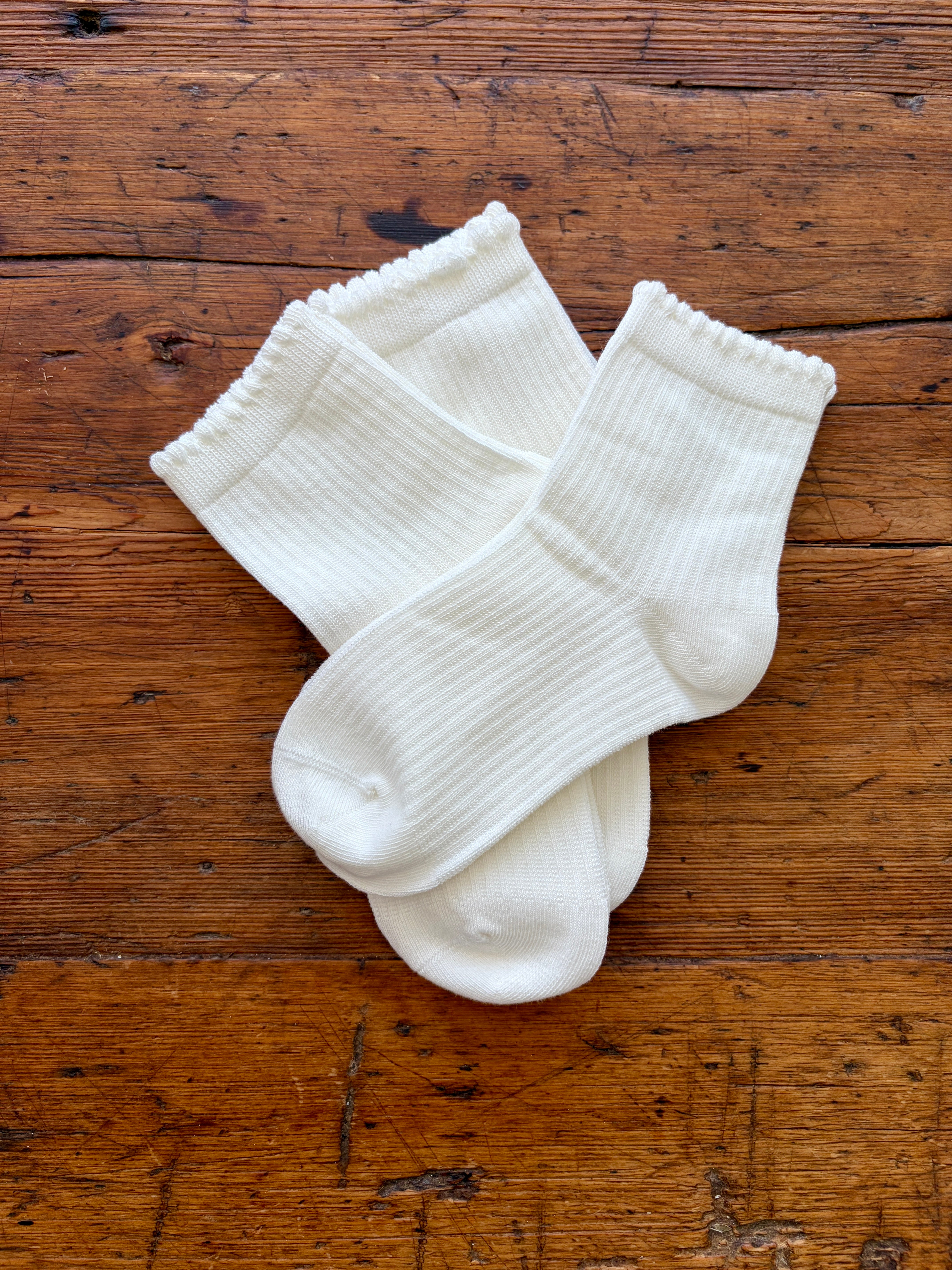 Three pairs of white ribbed ankle socks arranged on a rustic brown wooden surface.