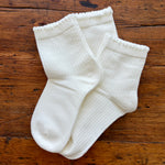 A pair of white ribbed ankle socks laid flat on a rustic brown wooden surface.