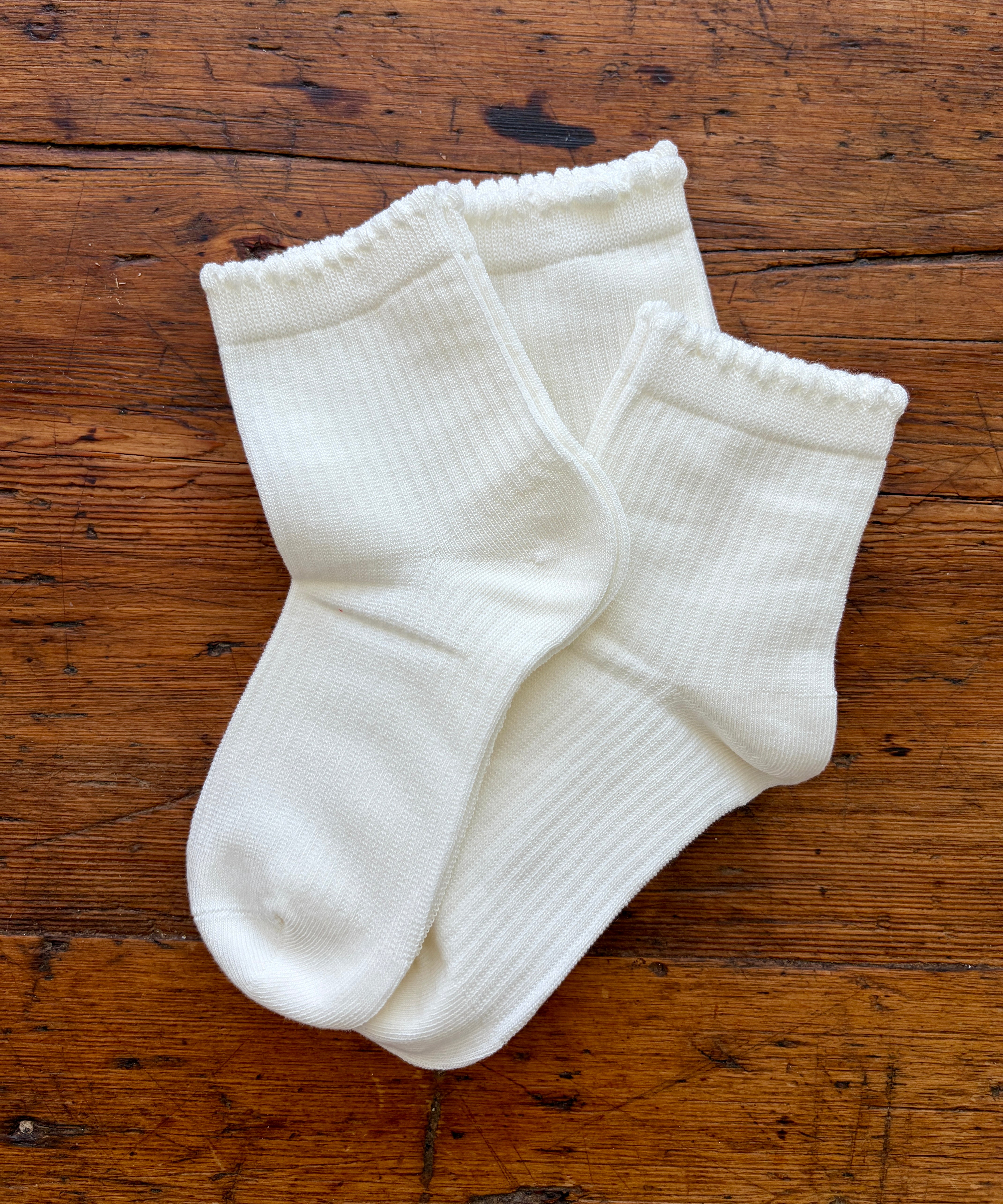 A pair of white ribbed ankle socks laid flat on a rustic brown wooden surface.