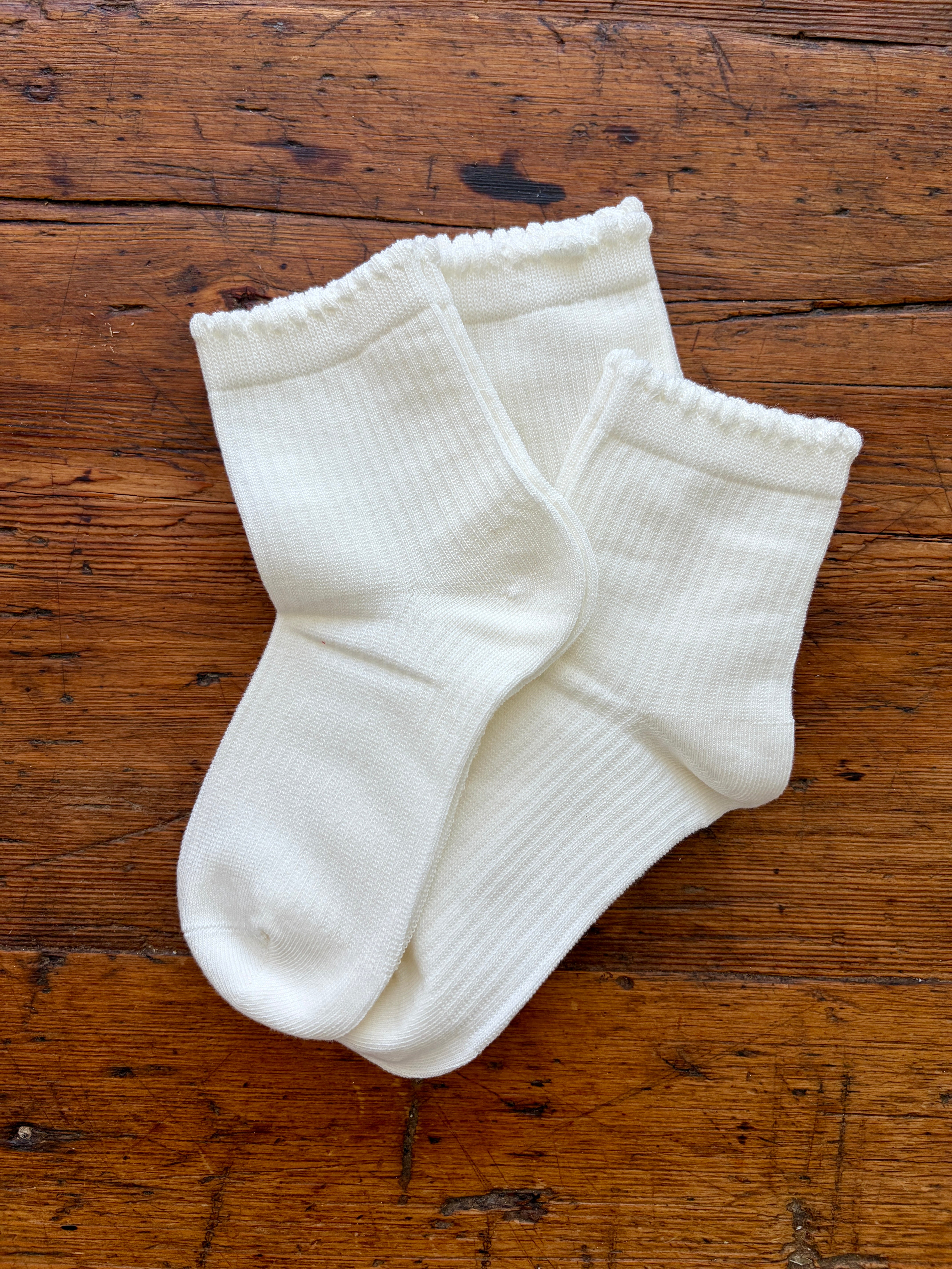 A pair of white ribbed ankle socks laid flat on a rustic brown wooden surface.